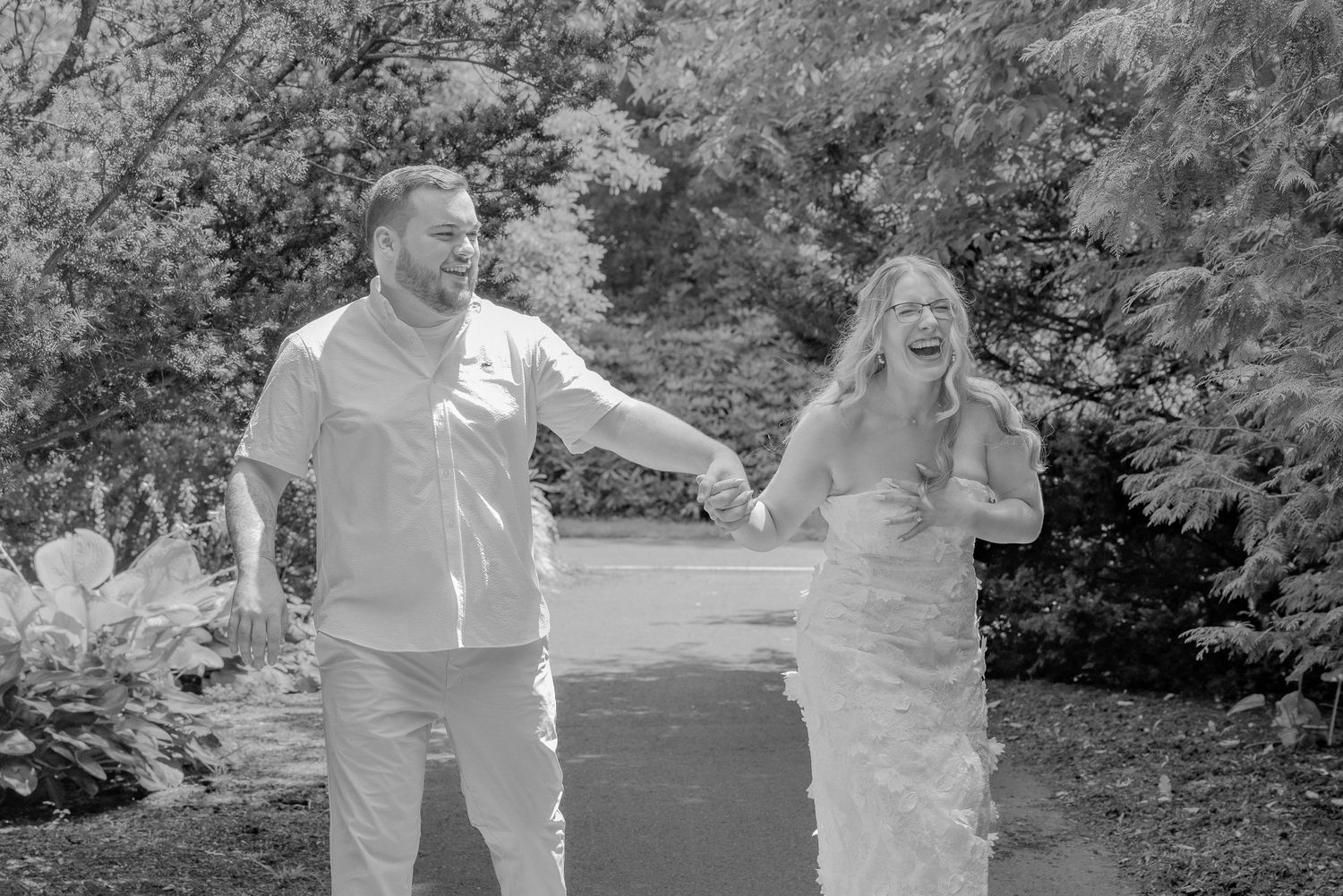 A black and white photograph of a couple walking and laughing together in a garden setting.