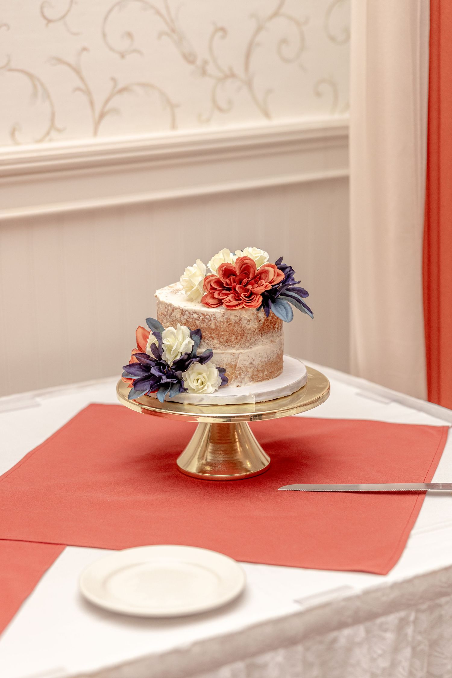 Small wedding cake decorated with fresh flowers on a gold cake stand.