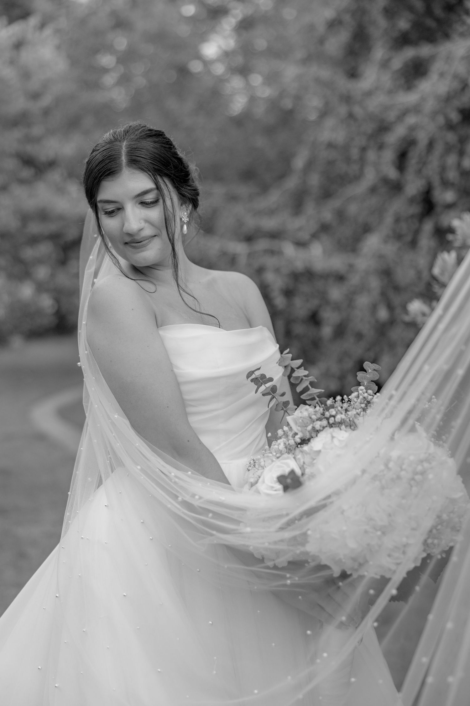 Black and white portrait of a bride in a flowing veil and strapless gown.