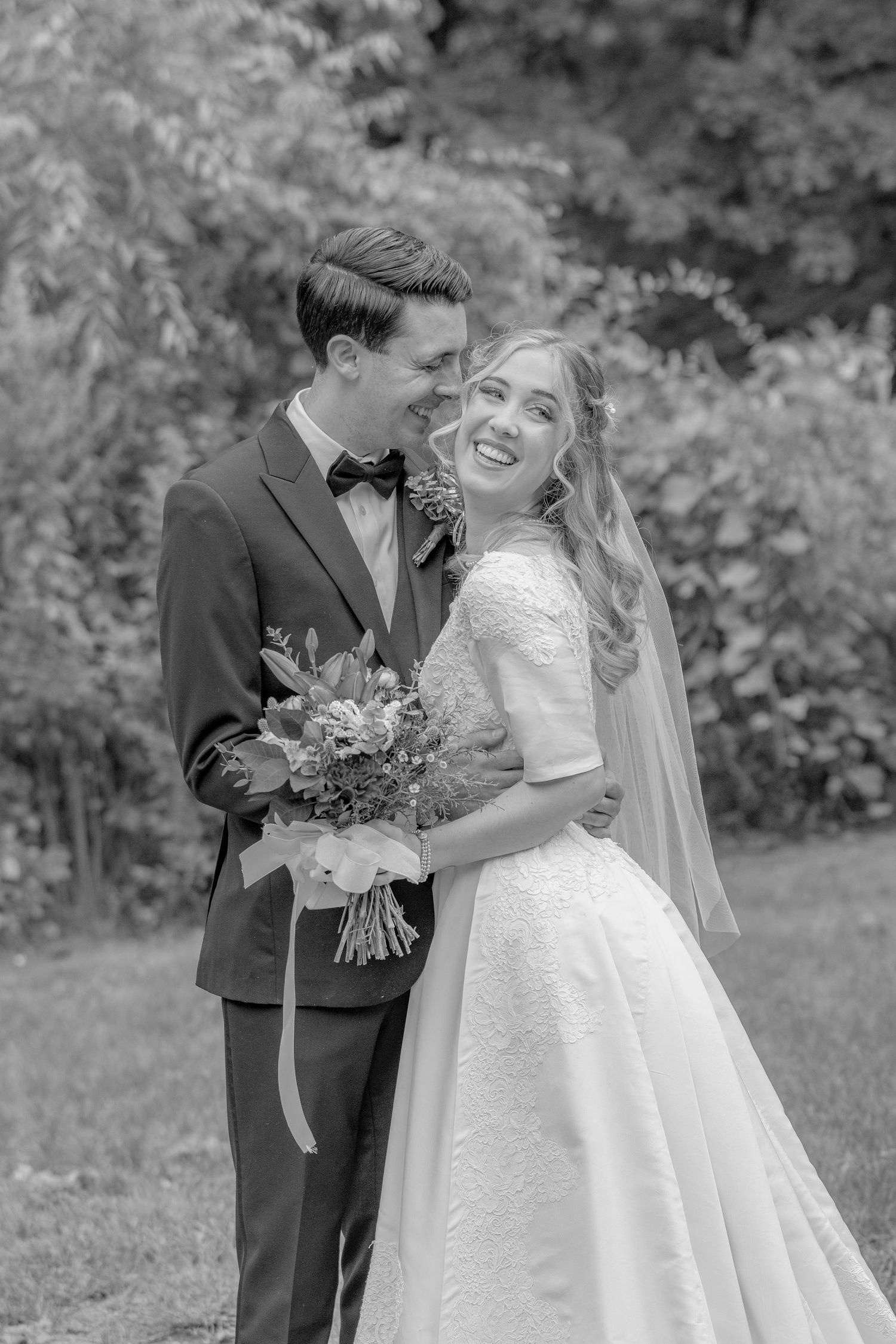 Black and white portrait of couple with bouquet in outdoor setting.
