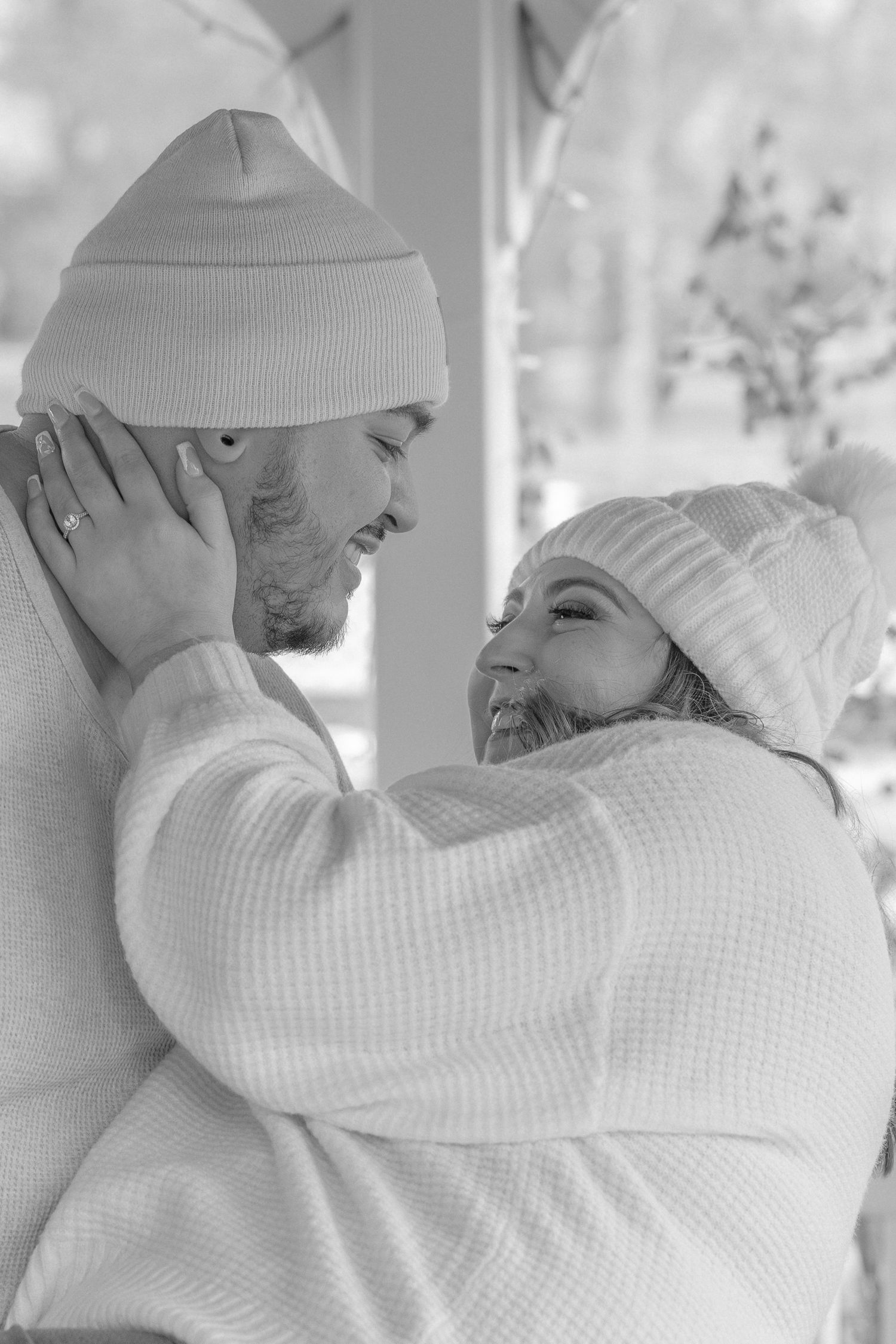 A tender black and white portrait of a couple embracing while wearing matching winter beanies.