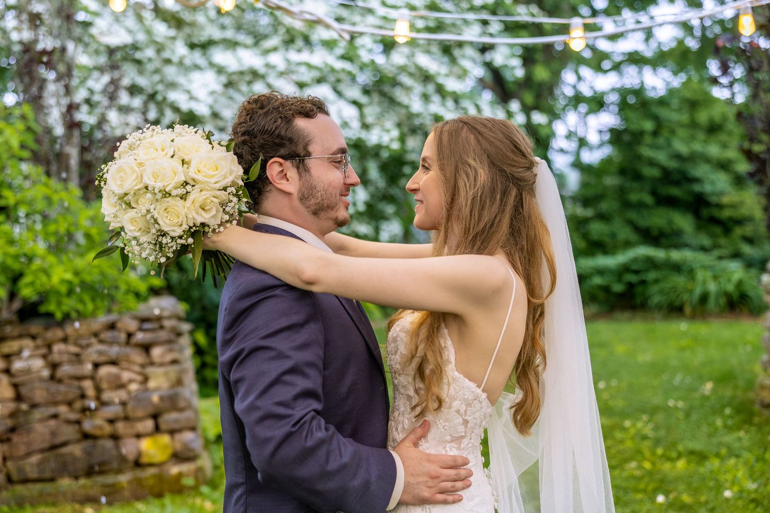 A couple in formal wedding attire share an intimate moment in a lush garden setting.