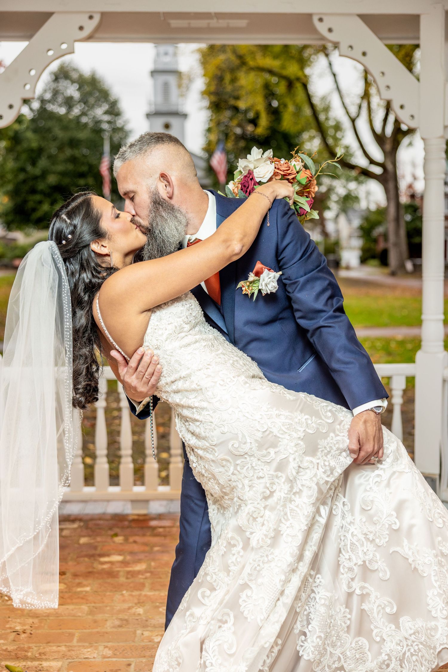 Newlyweds sharing a romantic dip kiss under a white gazebo.