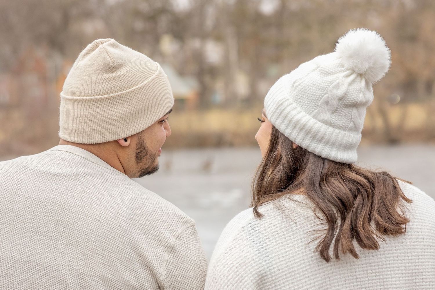A couple wearing winter knit hats and cozy sweaters sitting close together on a chilly day.