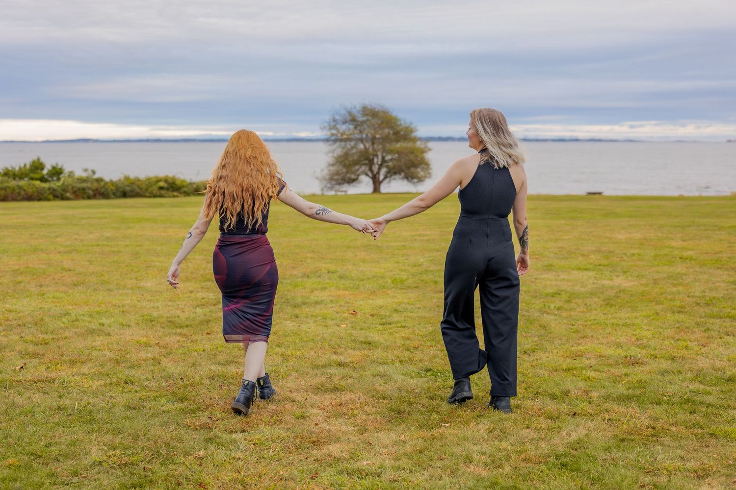 Two people holding hands while walking through a coastal meadow with ocean views.