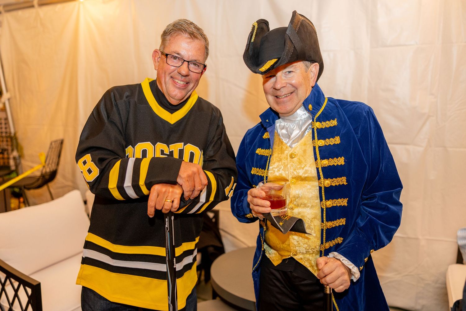 Two costumed guests in sports jersey and colonial outfit pose at party.