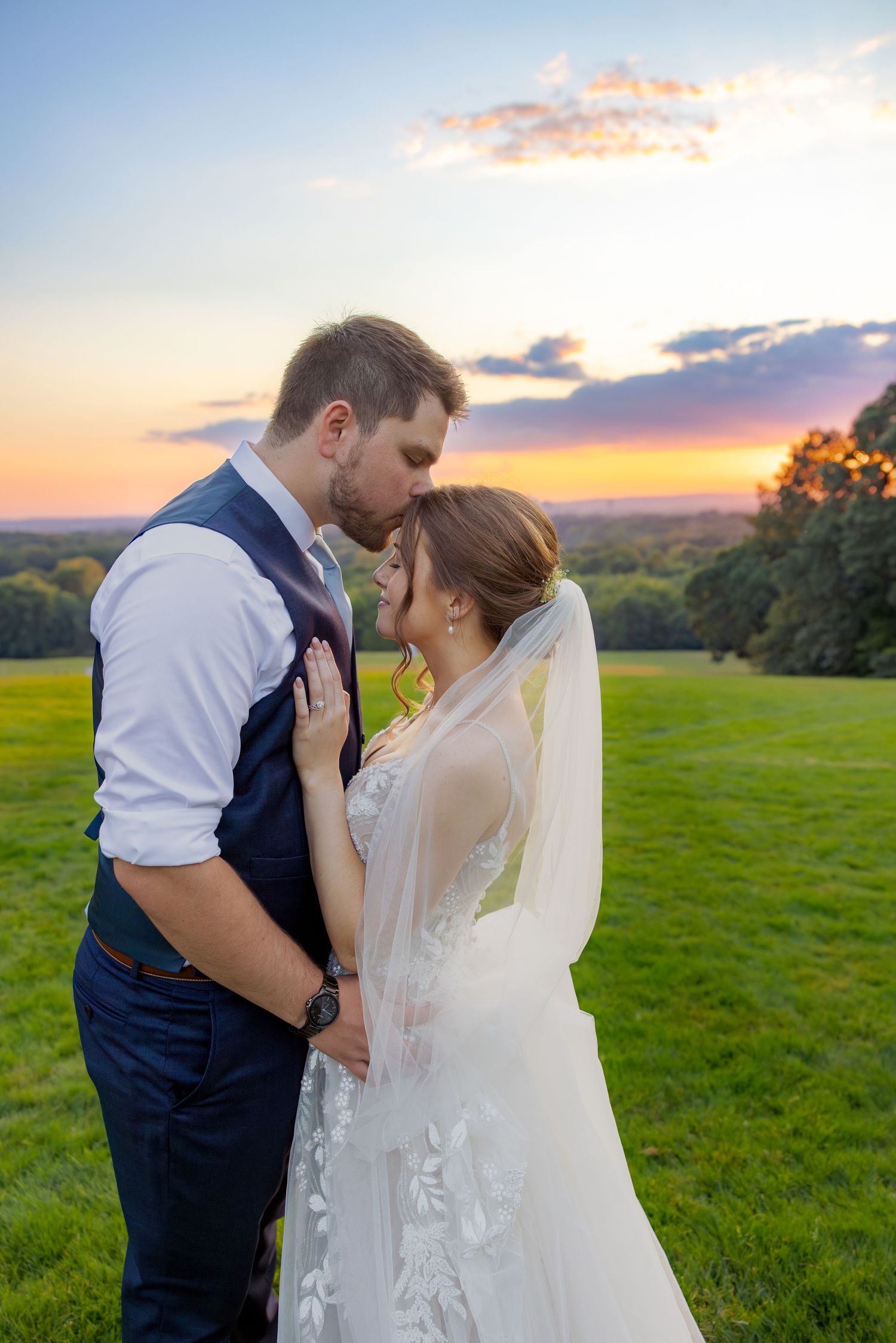 Intimate sunset wedding portrait with couple embracing on hilltop meadow.