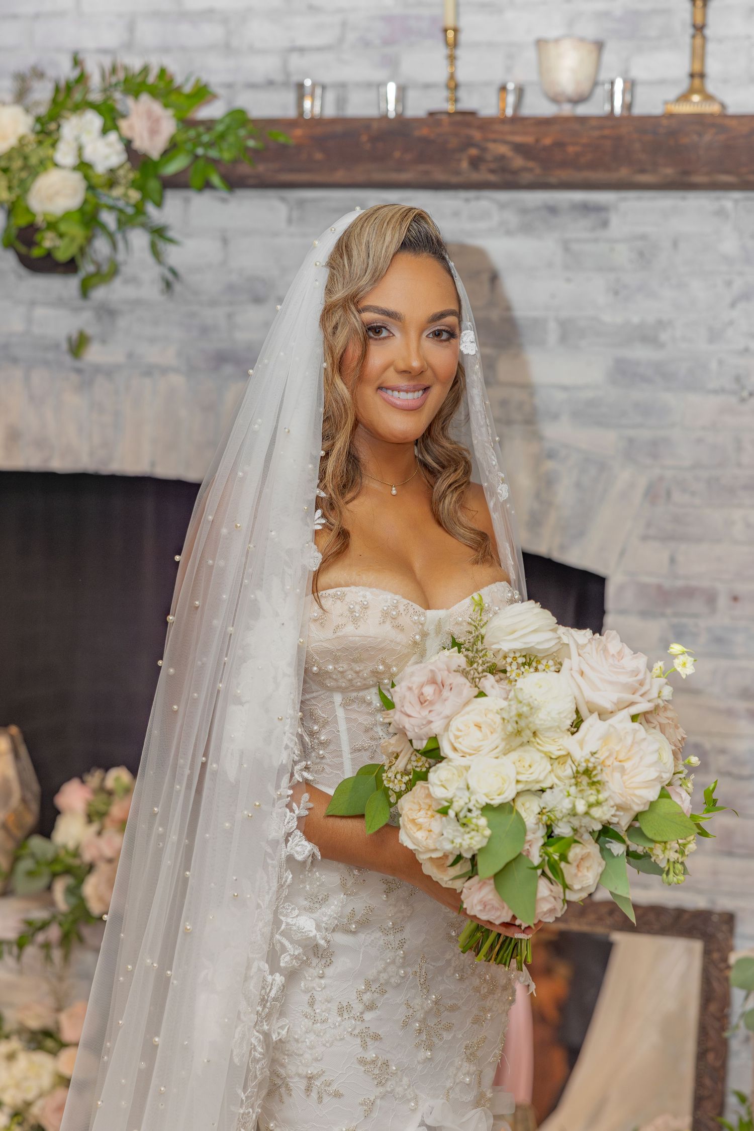 Beautiful bride holding white and blush bouquet against grey brick wall.