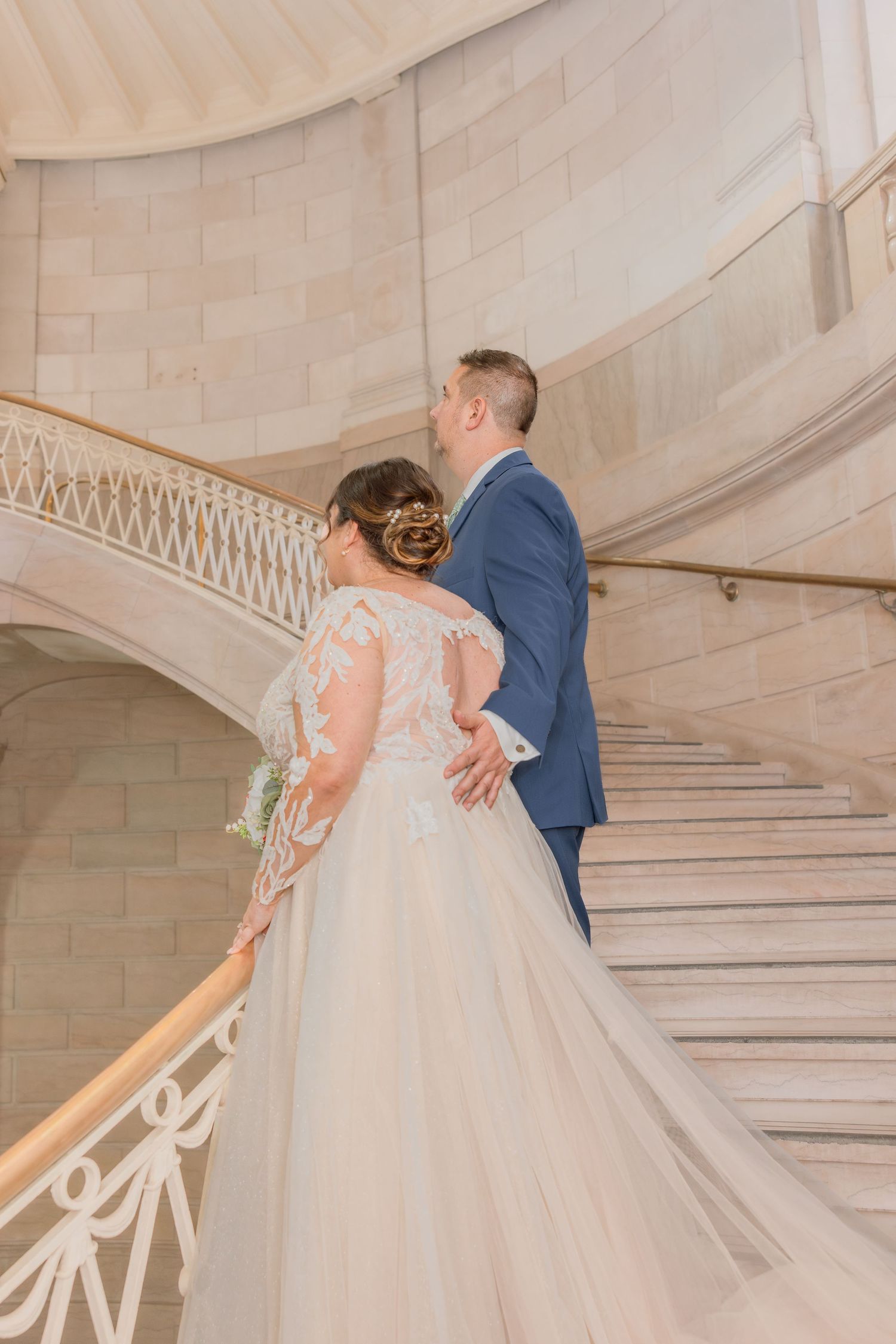 Couple poses on grand marble staircase during wedding photoshoot.
