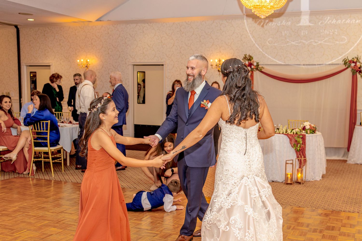 Wedding guests dancing together in a reception hall with warm lighting.