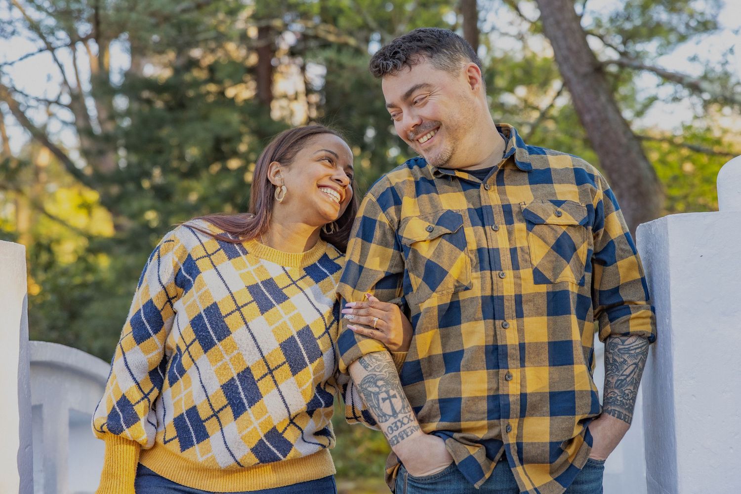 A couple in matching yellow and blue plaid patterns share a laugh together outdoors on a sunny day.