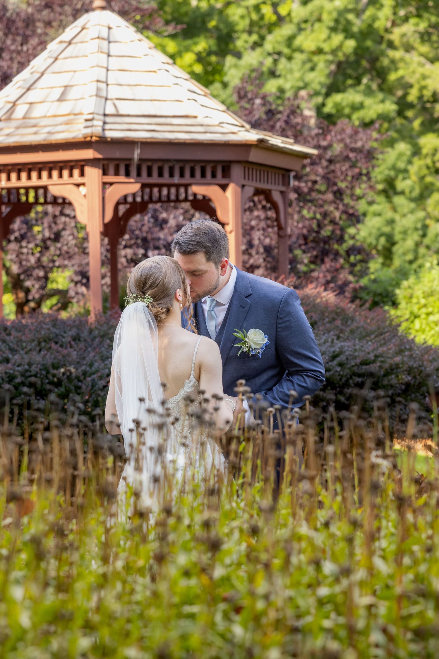 Intimate moment between newlyweds in front of a wooden gazebo surrounded by wildflowers.