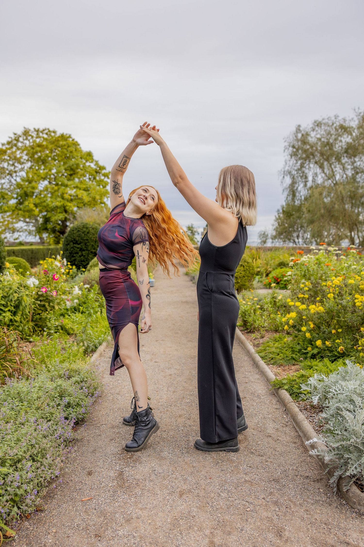 Two people dancing and twirling together on a garden path surrounded by blooming flowers.