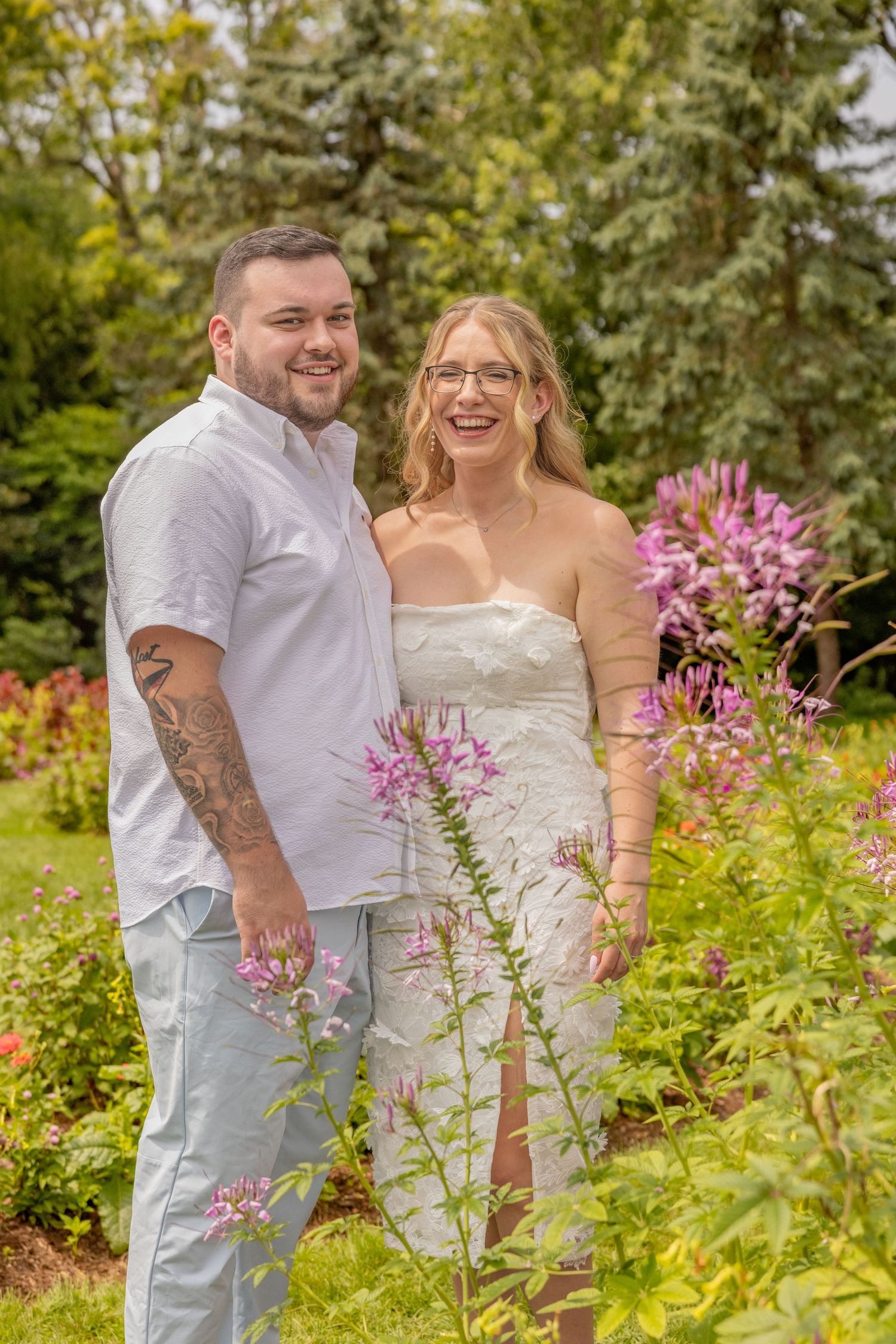 A happy couple posing among pink wildflowers in a vibrant summer garden.