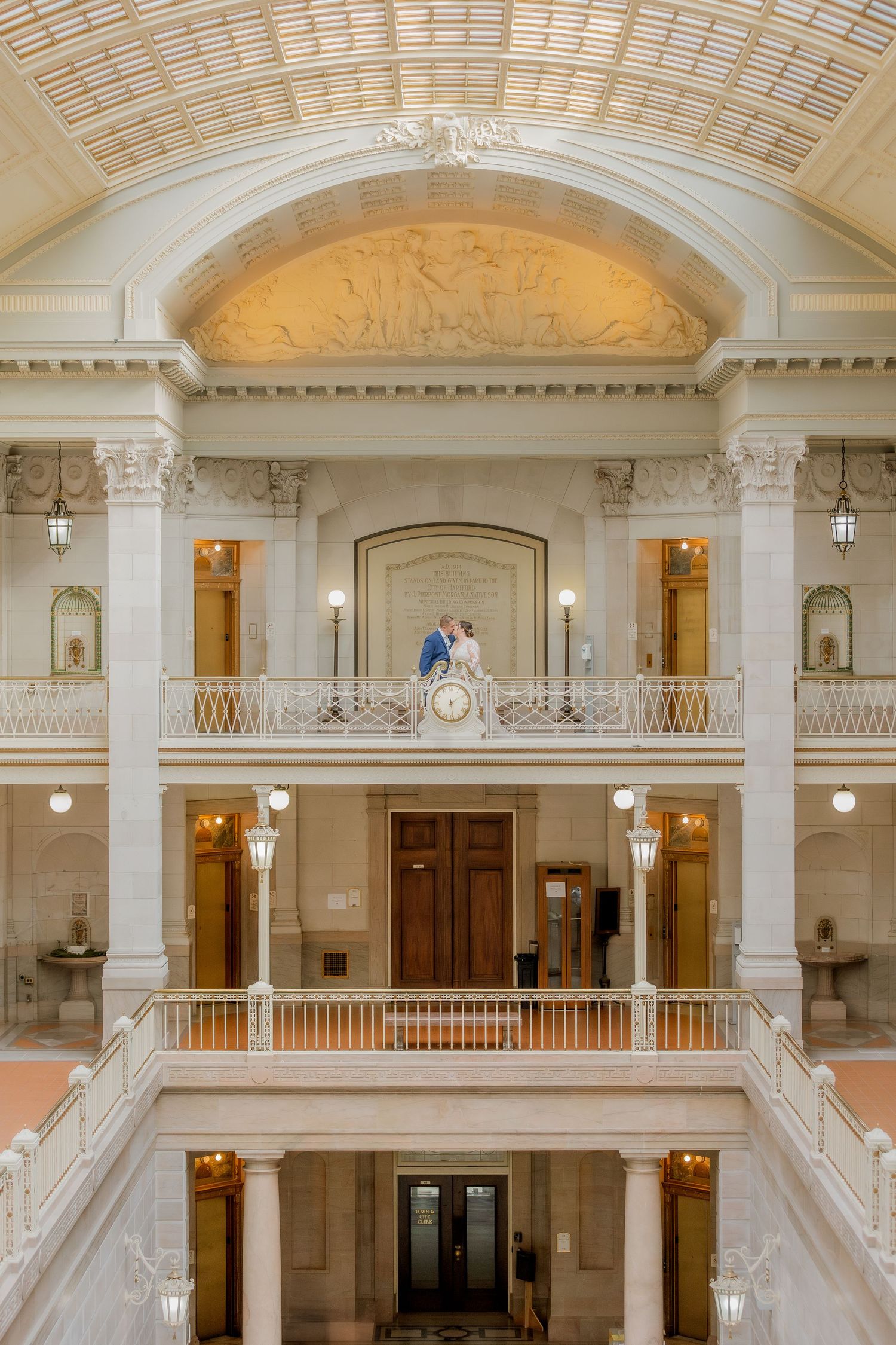 An elegant architectural interior features classical columns and multiple levels with a wedding scene.