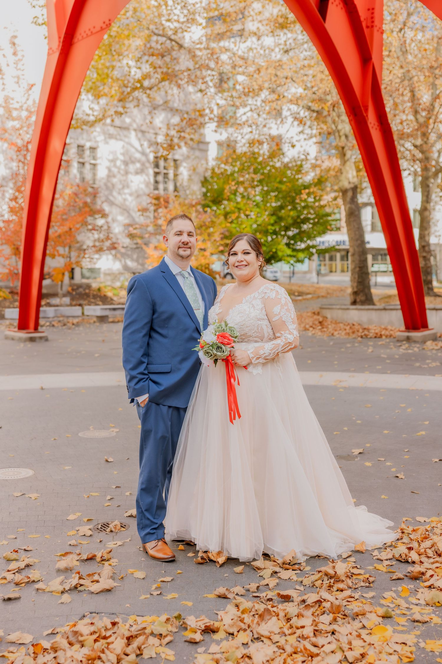Autumn wedding portrait under red metal sculpture with fallen leaves.