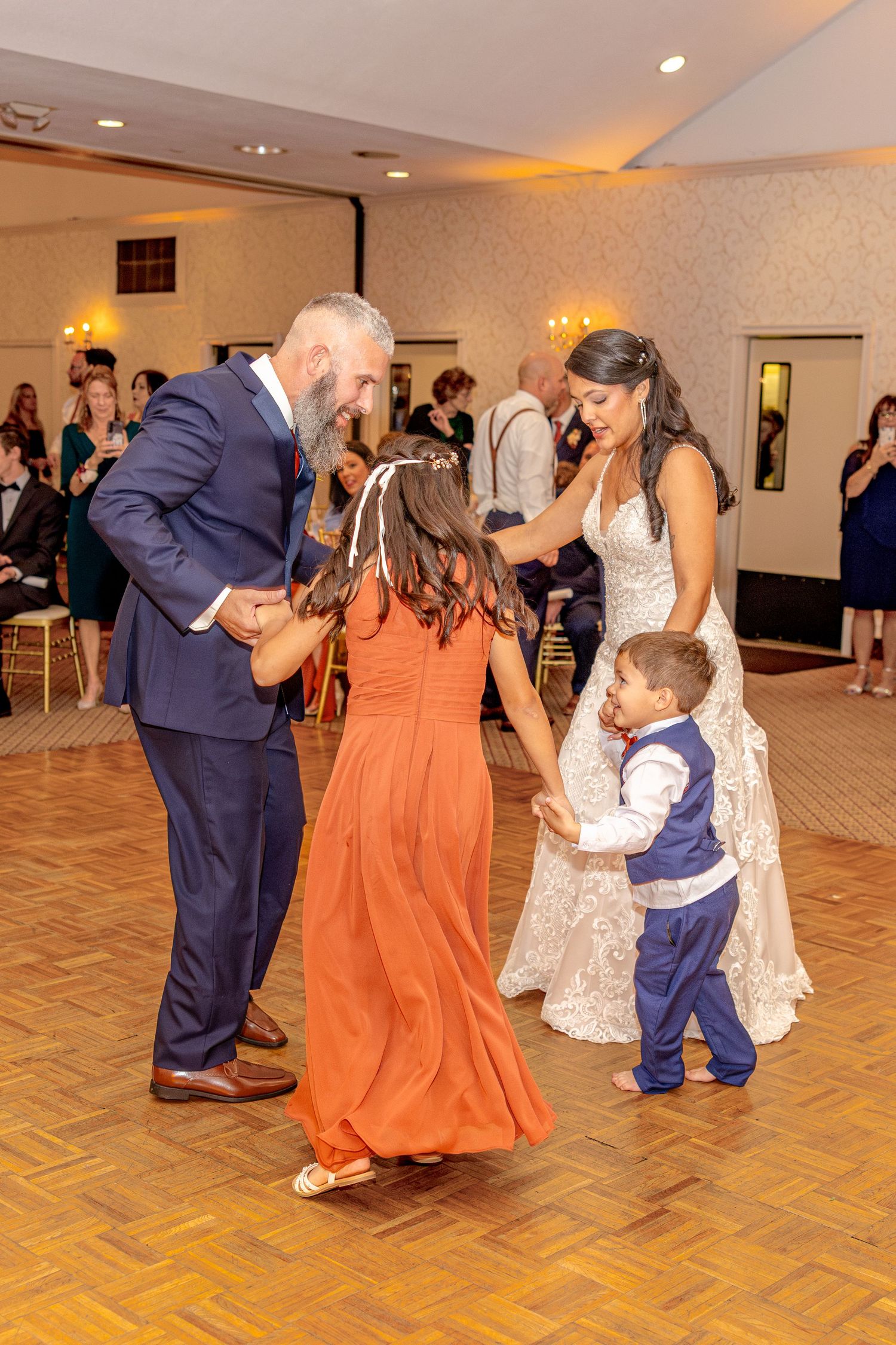 Wedding party dancing together on a parquet floor during reception celebrations.