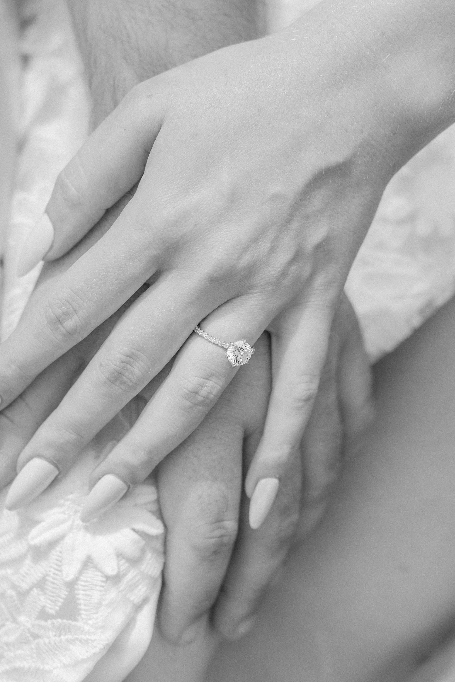 Close-up black and white photo of a bride's hand showing off an elegant diamond engagement ring.