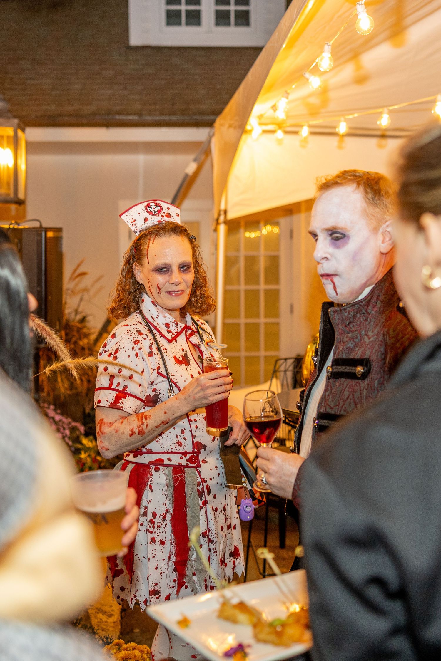 Halloween party guests in bloody nurse and ghostly makeup costumes socialize indoors.