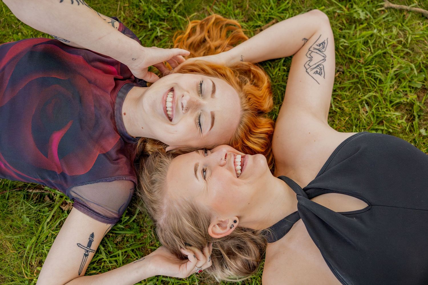 Two people lying in green grass with their heads together, smiling with pure joy.
