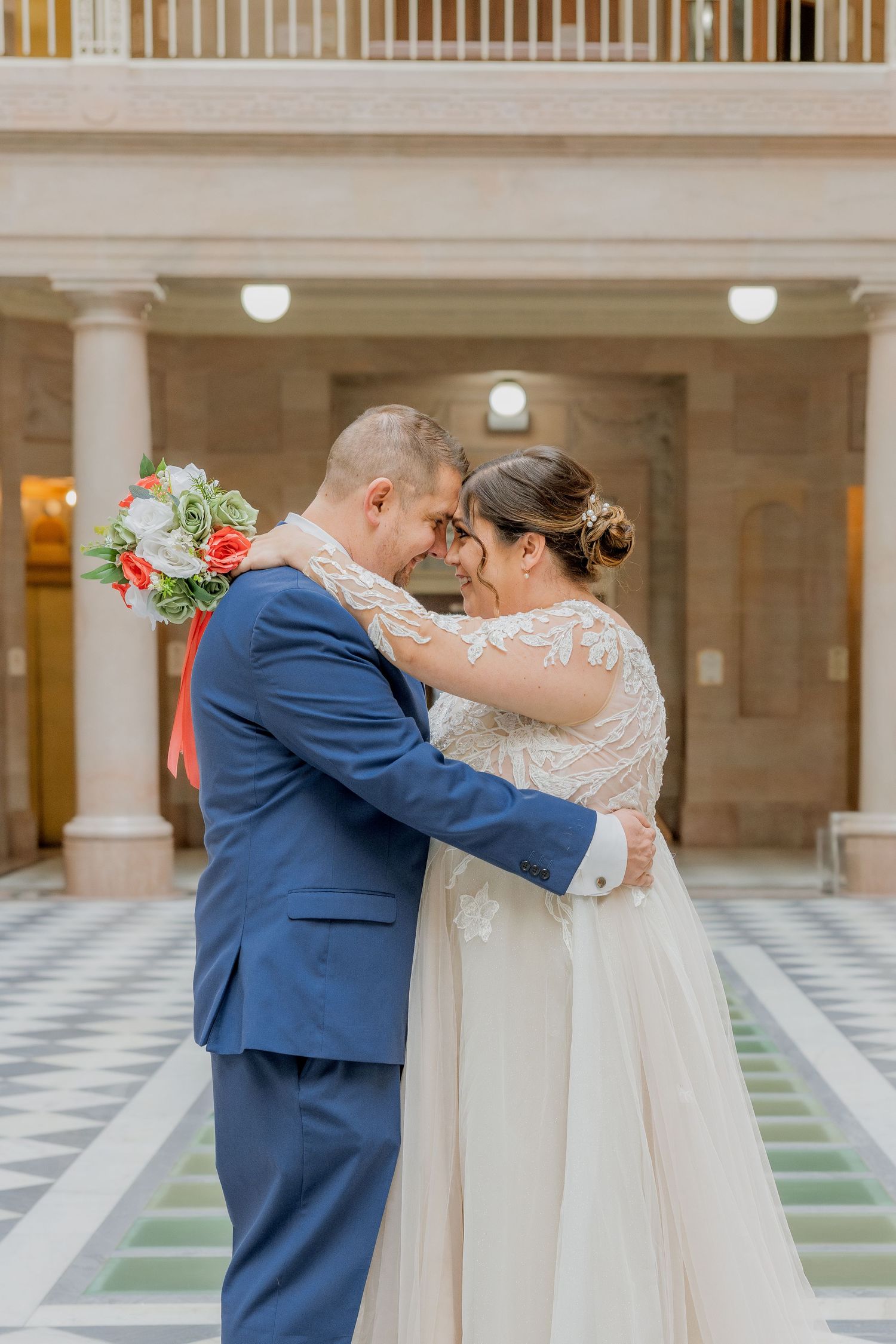 Tender moment between newlyweds in elegant attire under columned architecture.