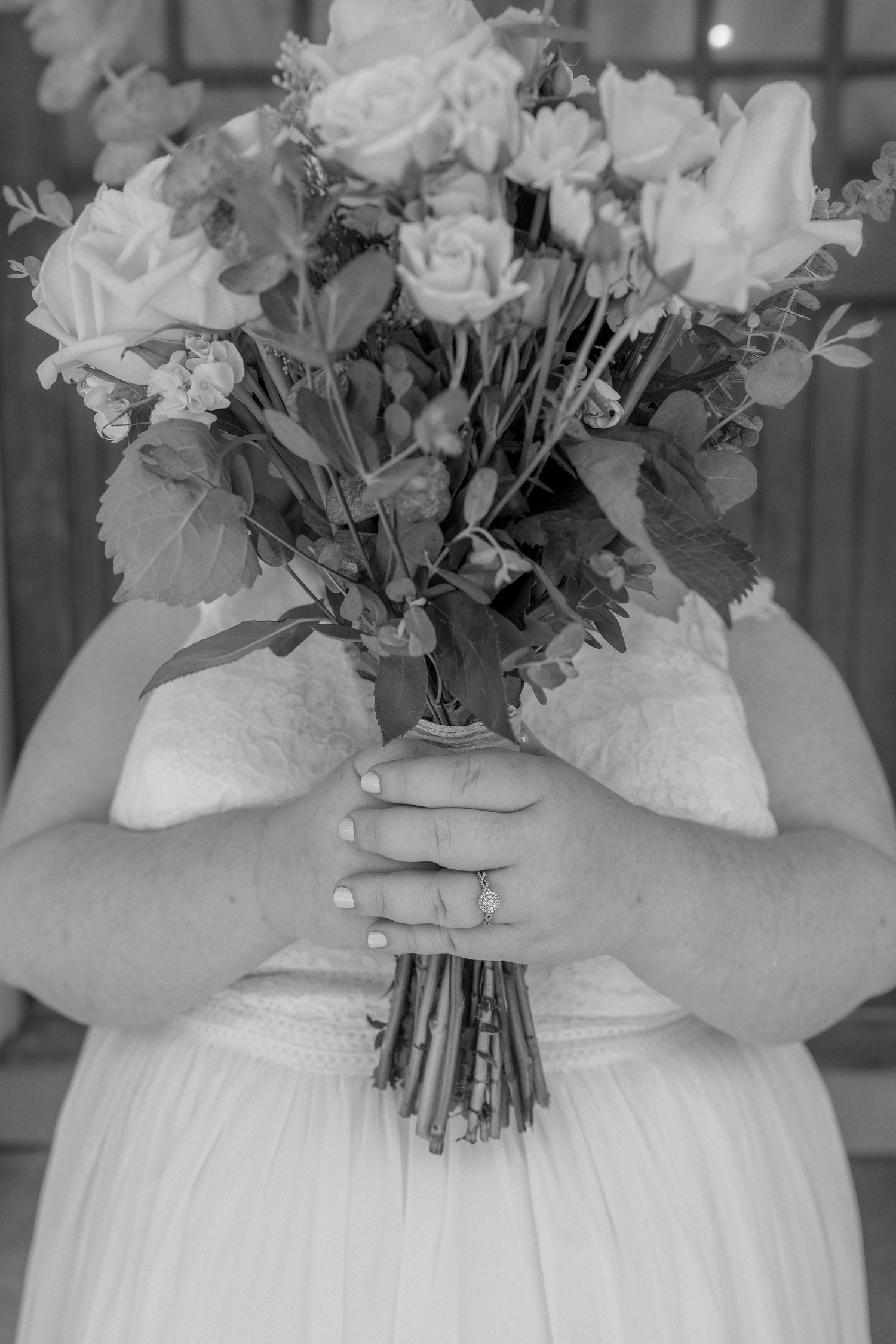 Close-up of bridal bouquet with white roses held against white wedding dress.