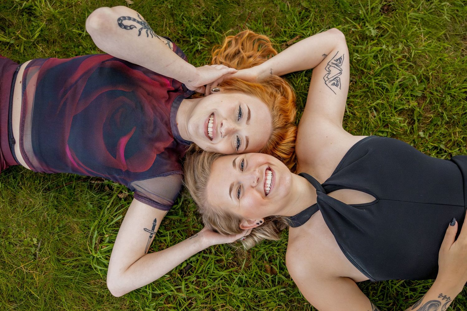 Two people lying on grass with their heads together, sharing genuine laughter and joy.