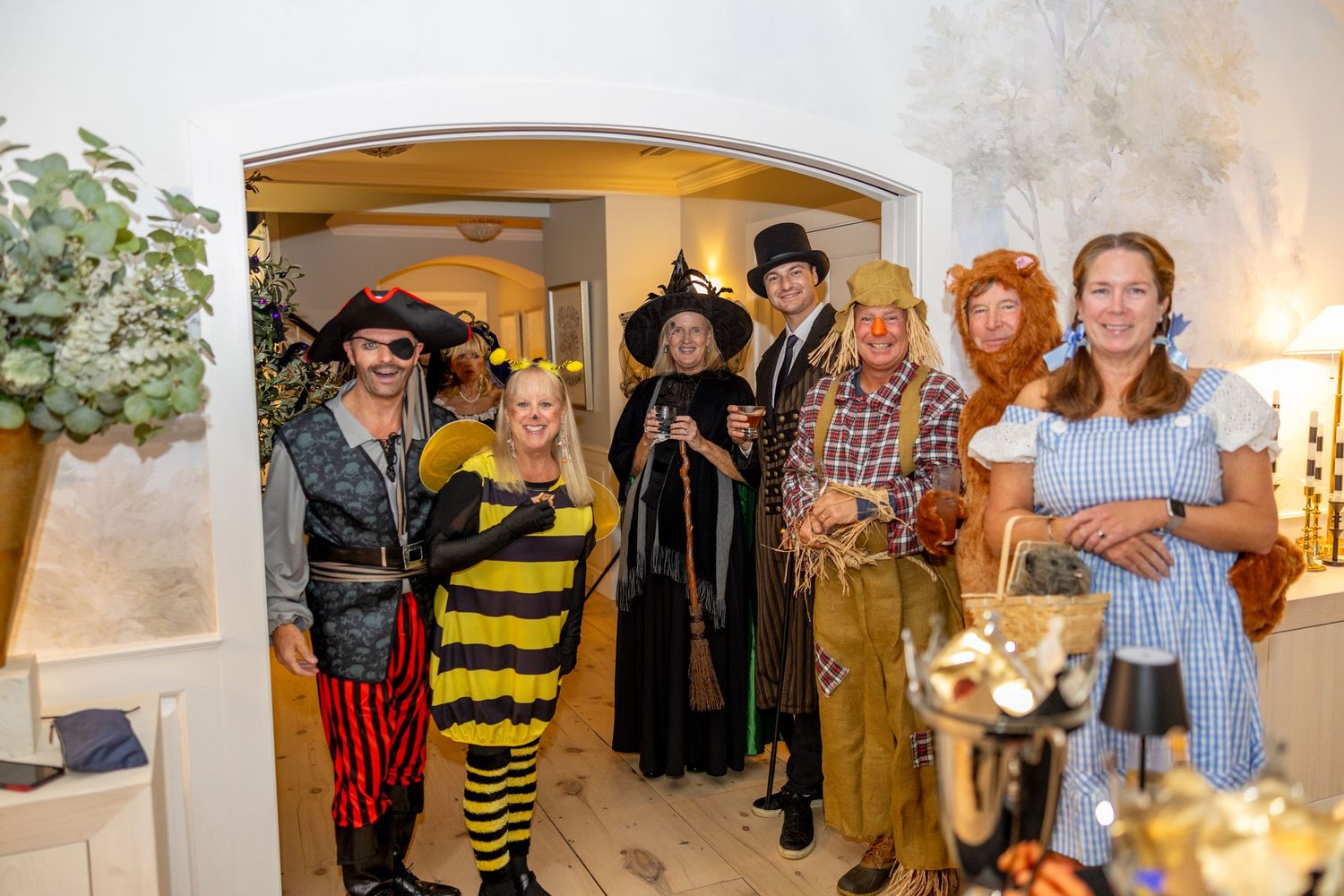 Group of people in various Halloween costumes including pirates and witches pose together indoors.