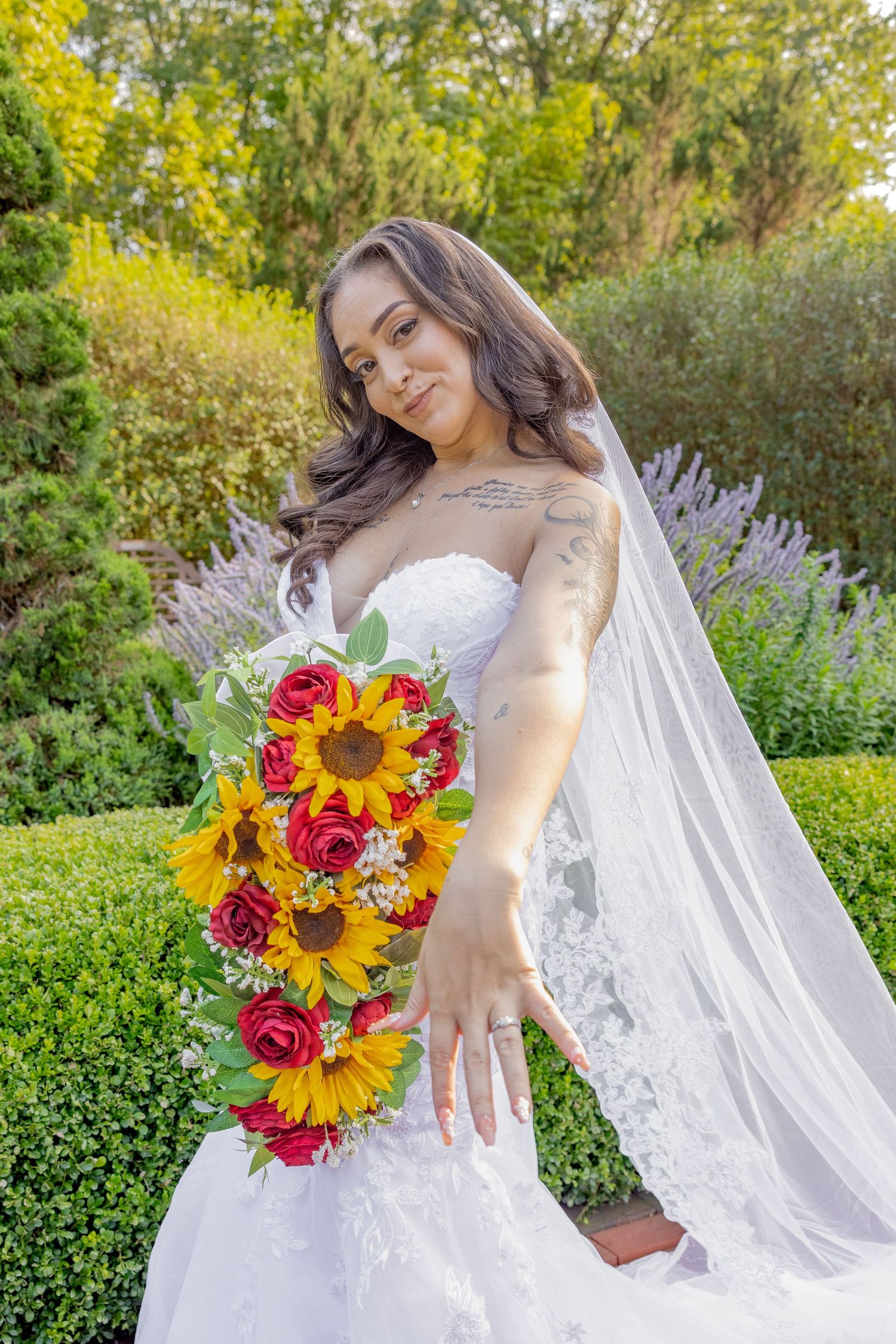 Bride in white dress poses with cascading sunflower bouquet in garden with lavender flowers.