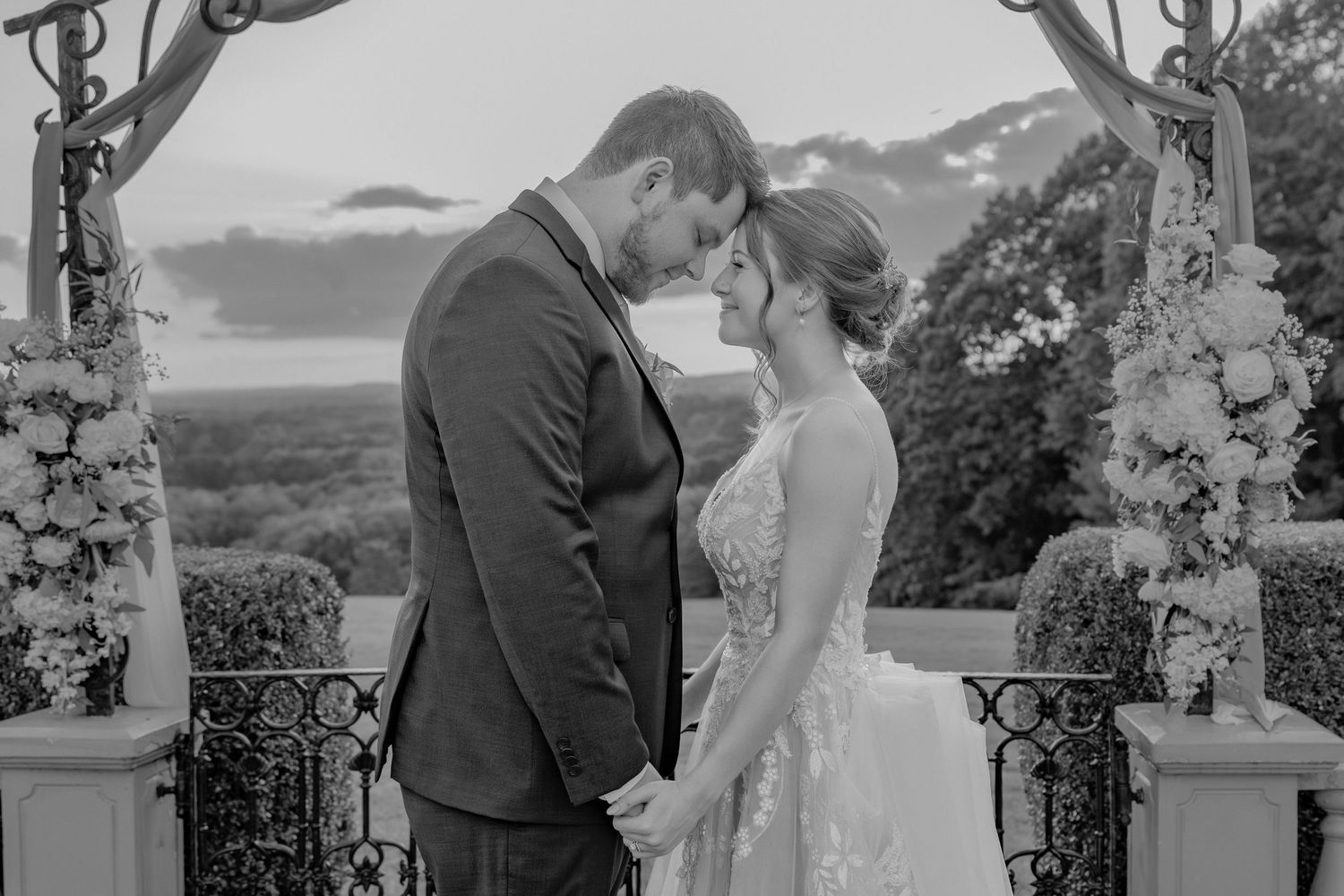 Couple shares intimate moment under floral arch with scenic mountain backdrop.