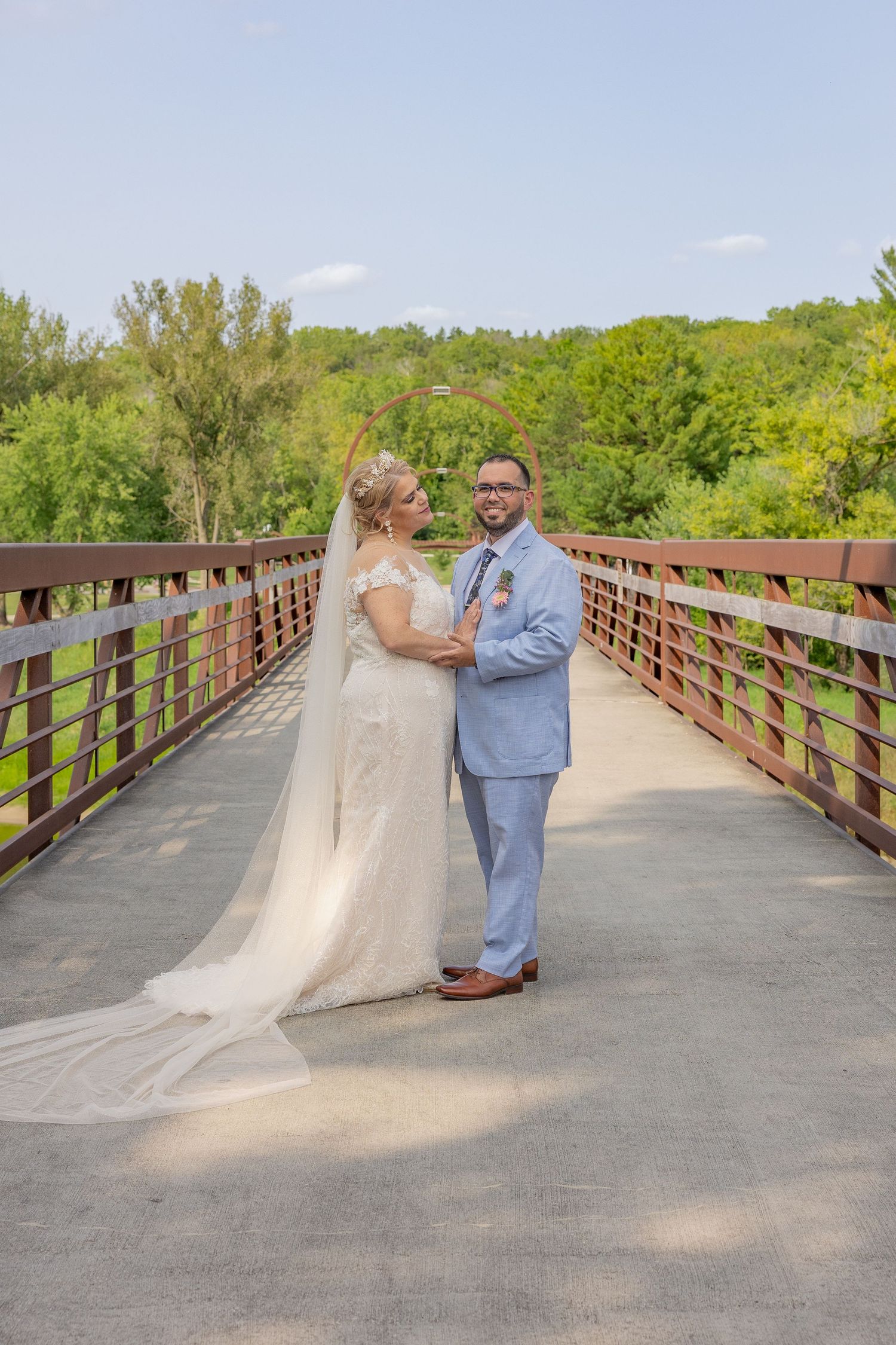Couple shares romantic moment on wooden bridge with lush greenery in background.