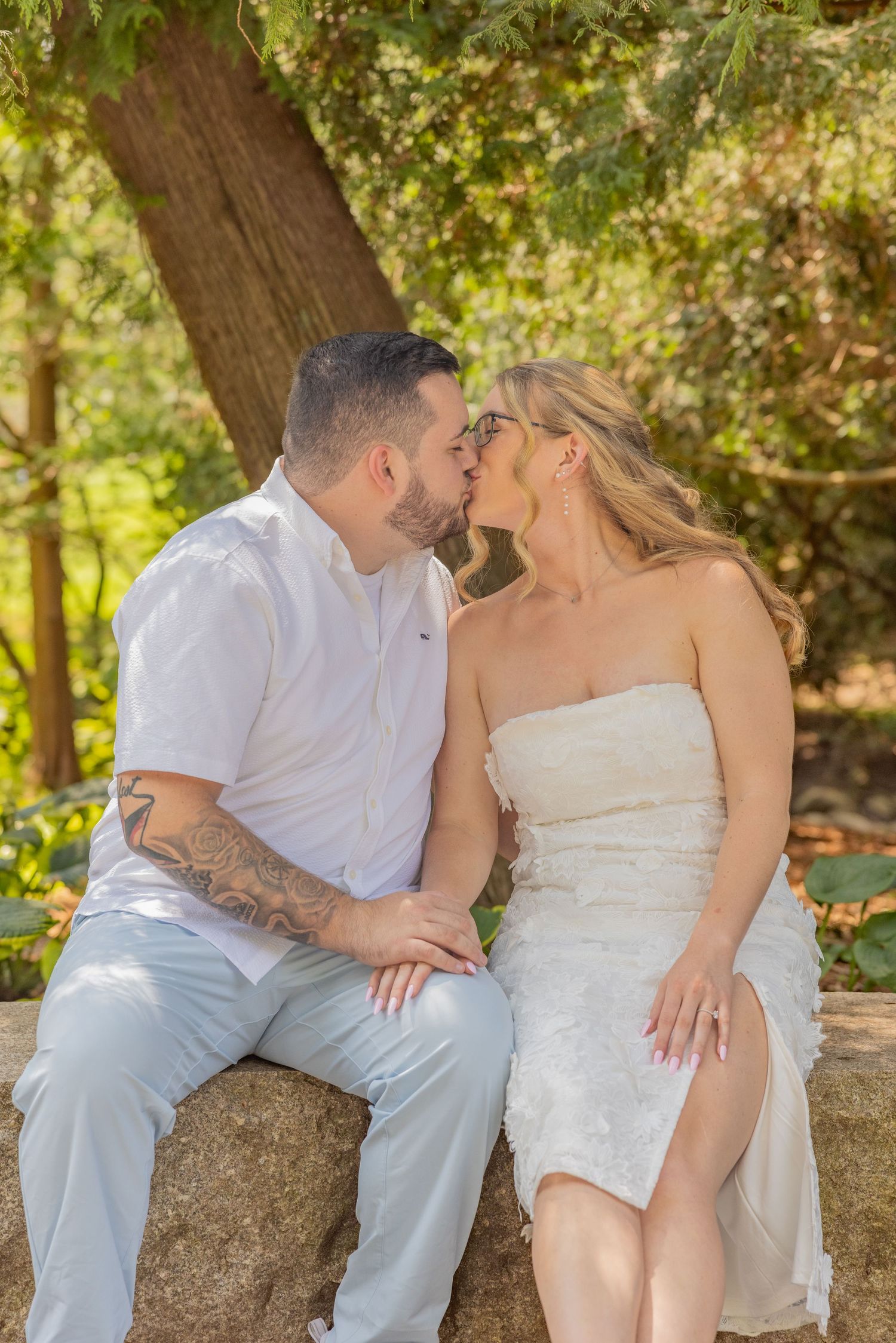 A romantic couple sharing an intimate moment while sitting on a stone wall in a garden setting.