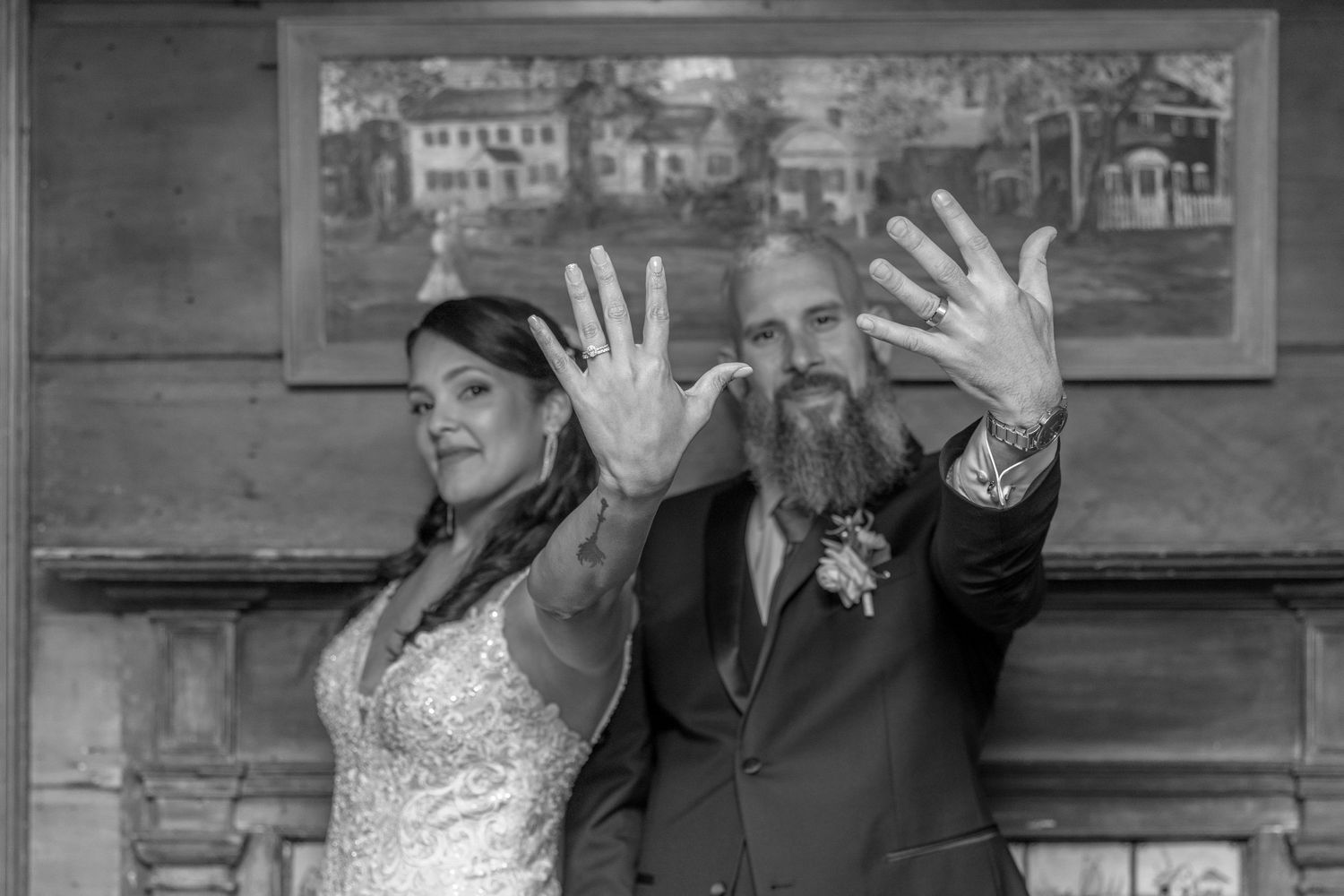 Newlyweds pose playfully with outstretched hands in a black and white photo.