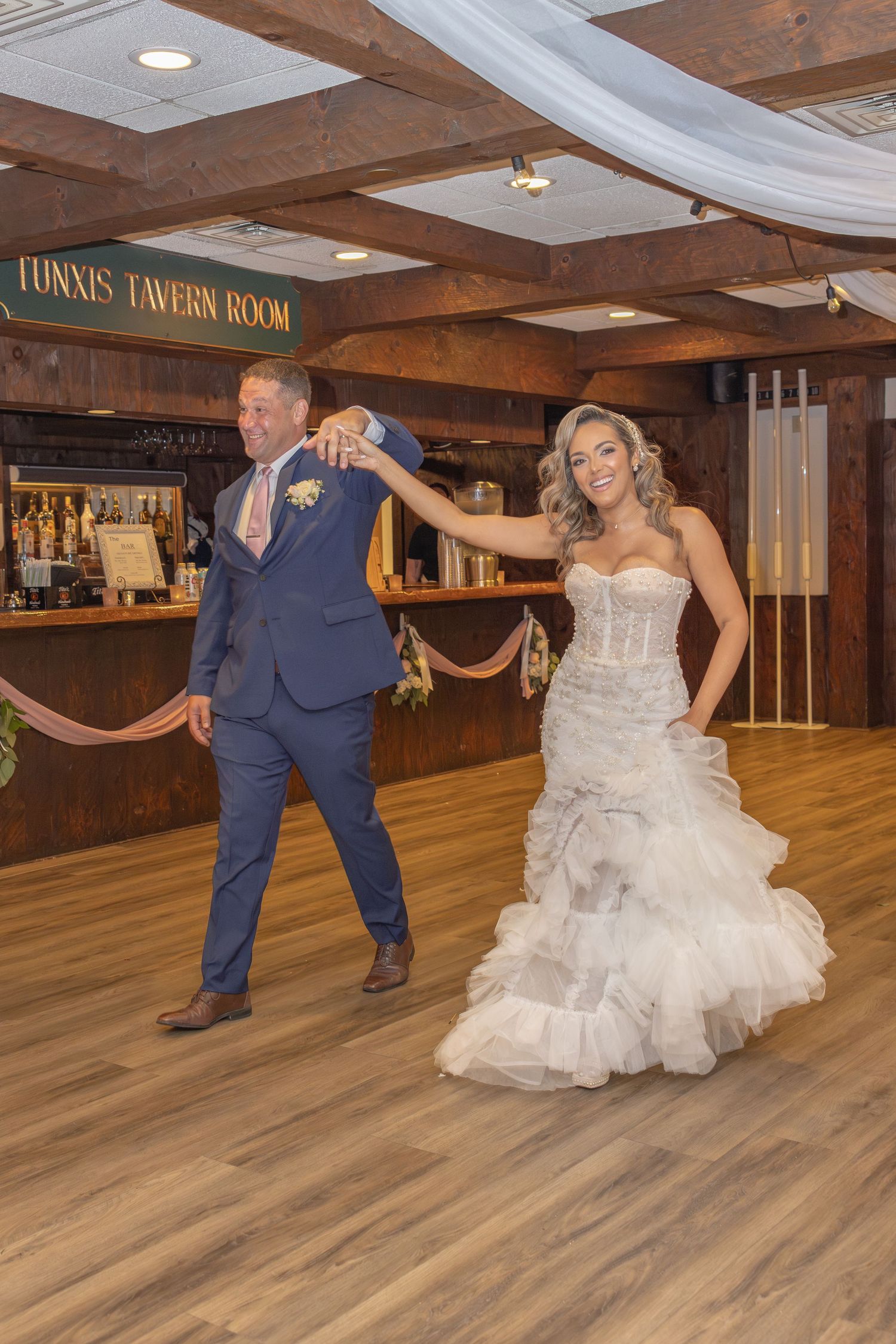 Wedding couple dances in rustic tavern room with wooden beams.