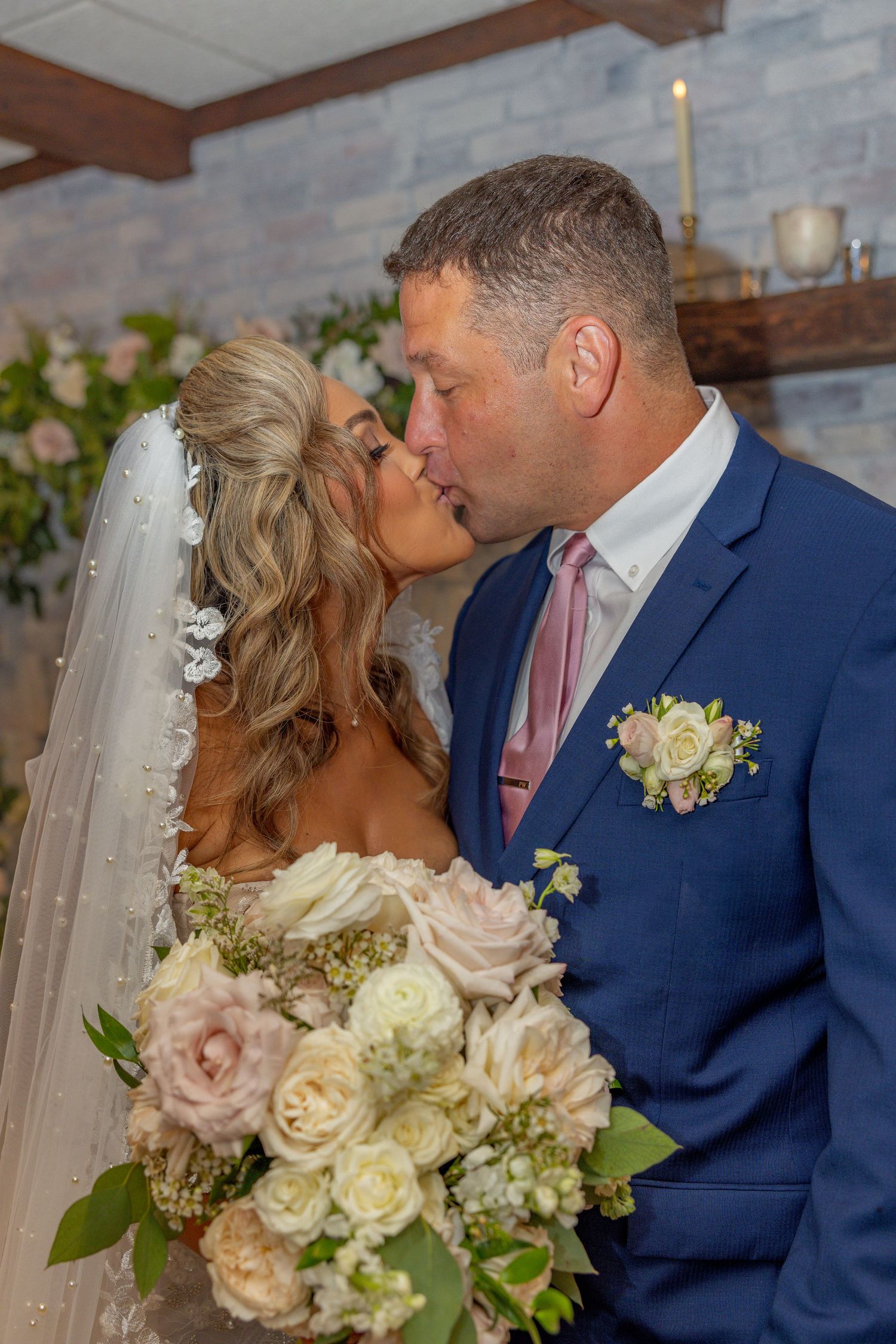 Wedding couple sharing a romantic kiss while holding a beautiful floral bouquet.