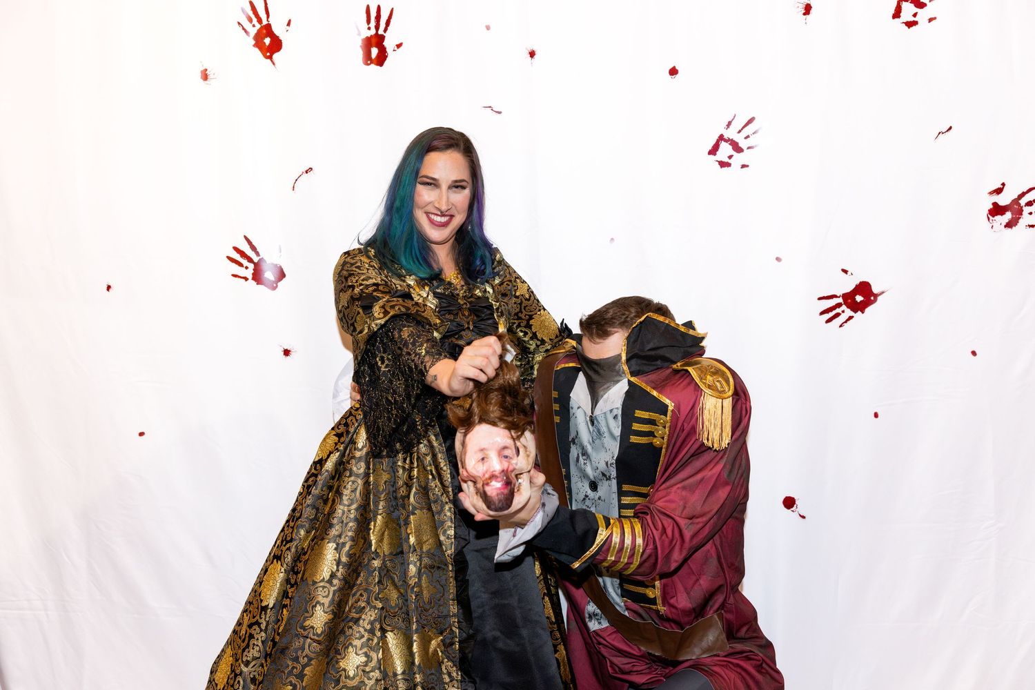 Group in renaissance costumes poses dramatically against white backdrop with red handprint decorations.
