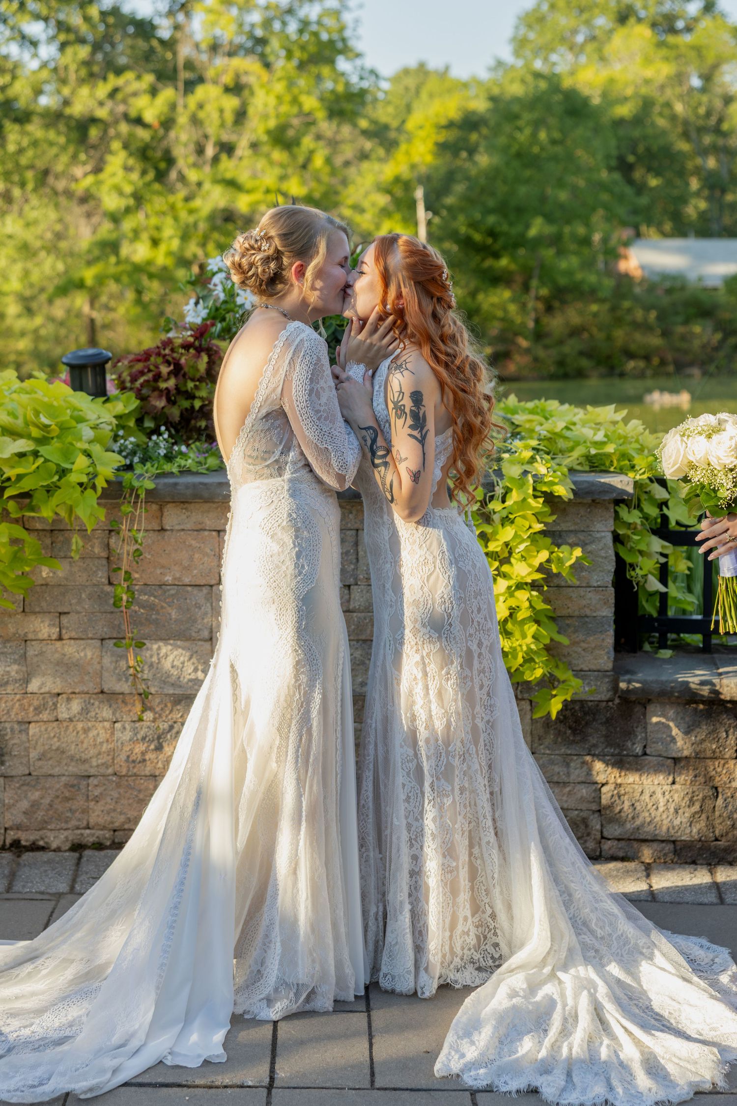A romantic wedding moment captured in a garden setting with stone walls and lush greenery in the background.