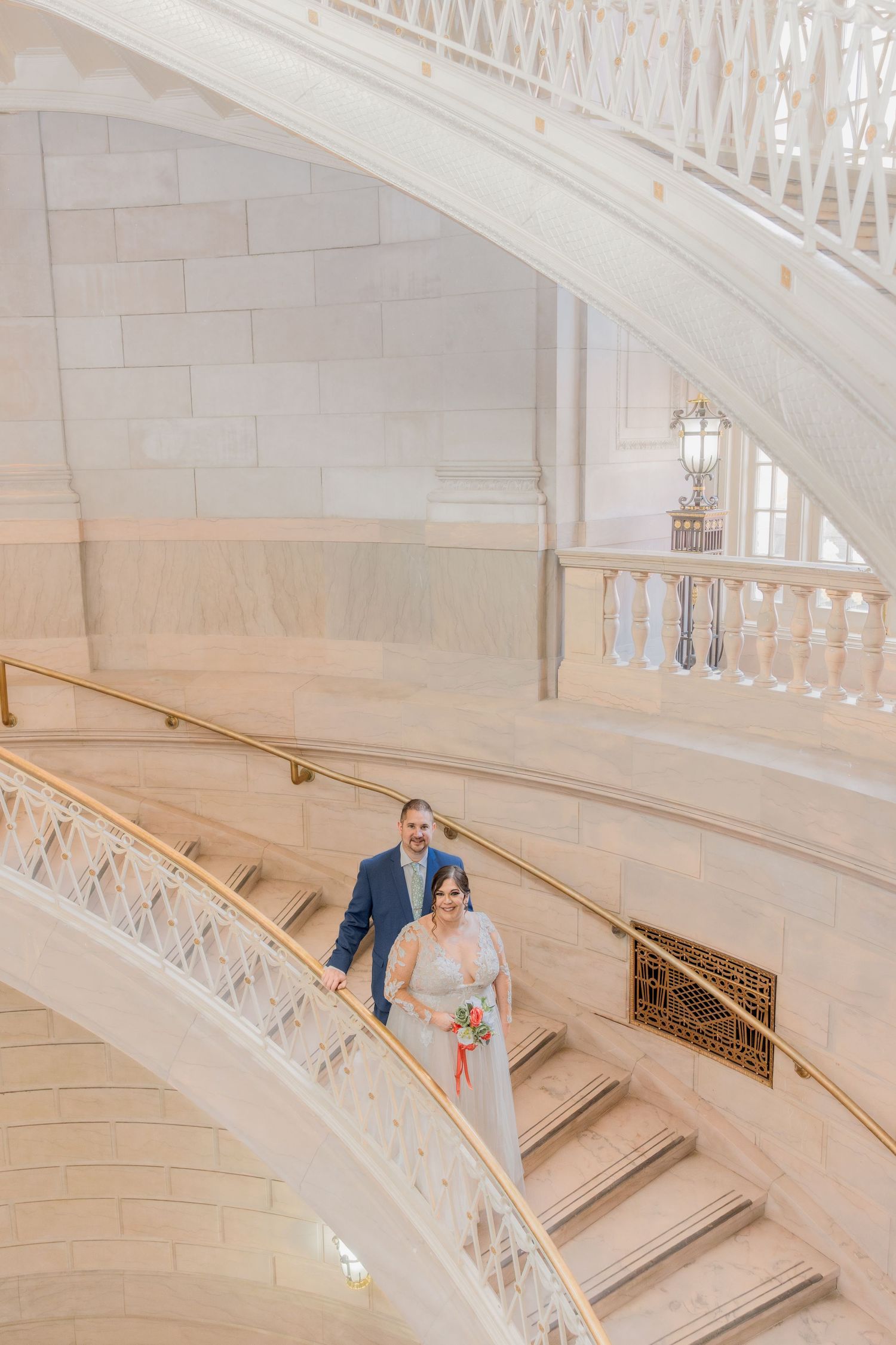 Wedding couple ascending an elegant white marble staircase in a grand building.