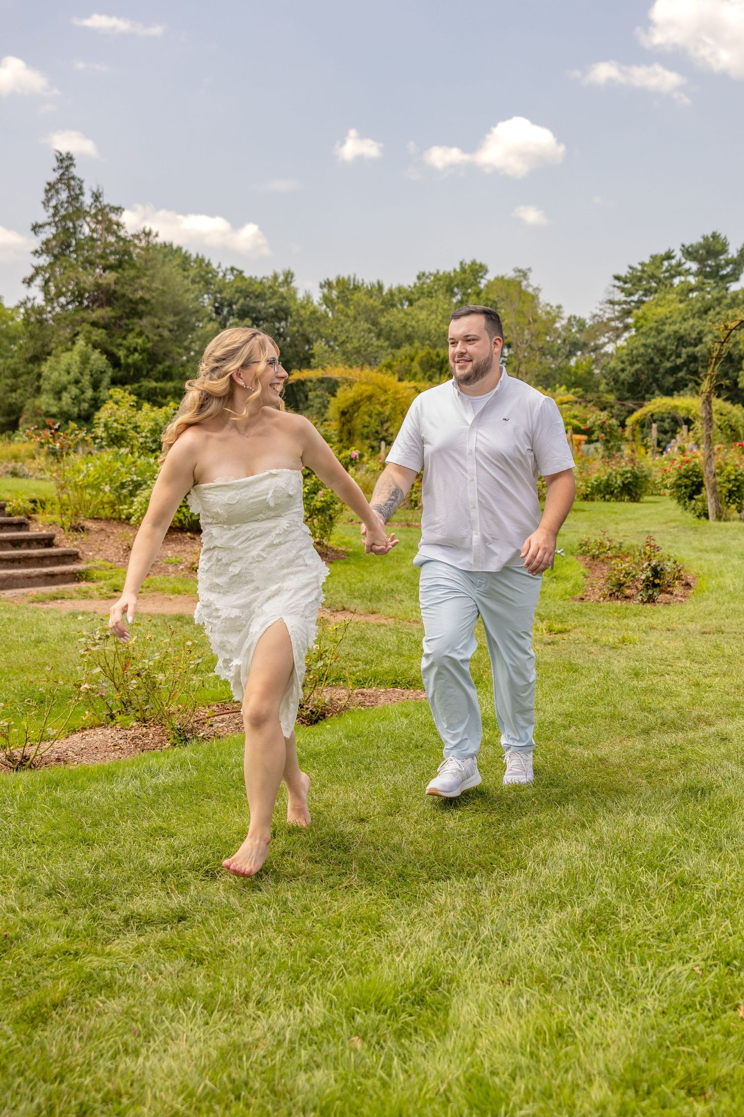 A couple running playfully through a summer garden with bright green grass.