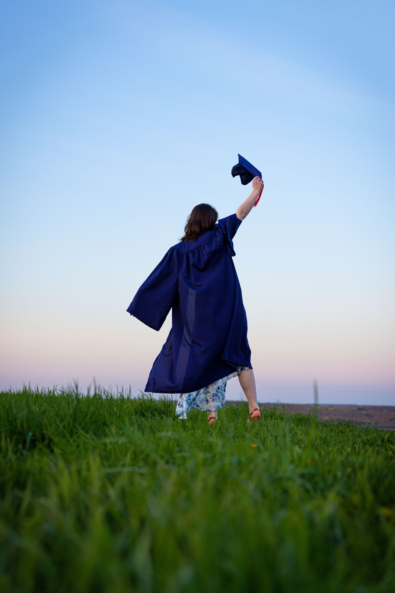 Silhouette of graduate holding cap triumphantly in field at sunset.