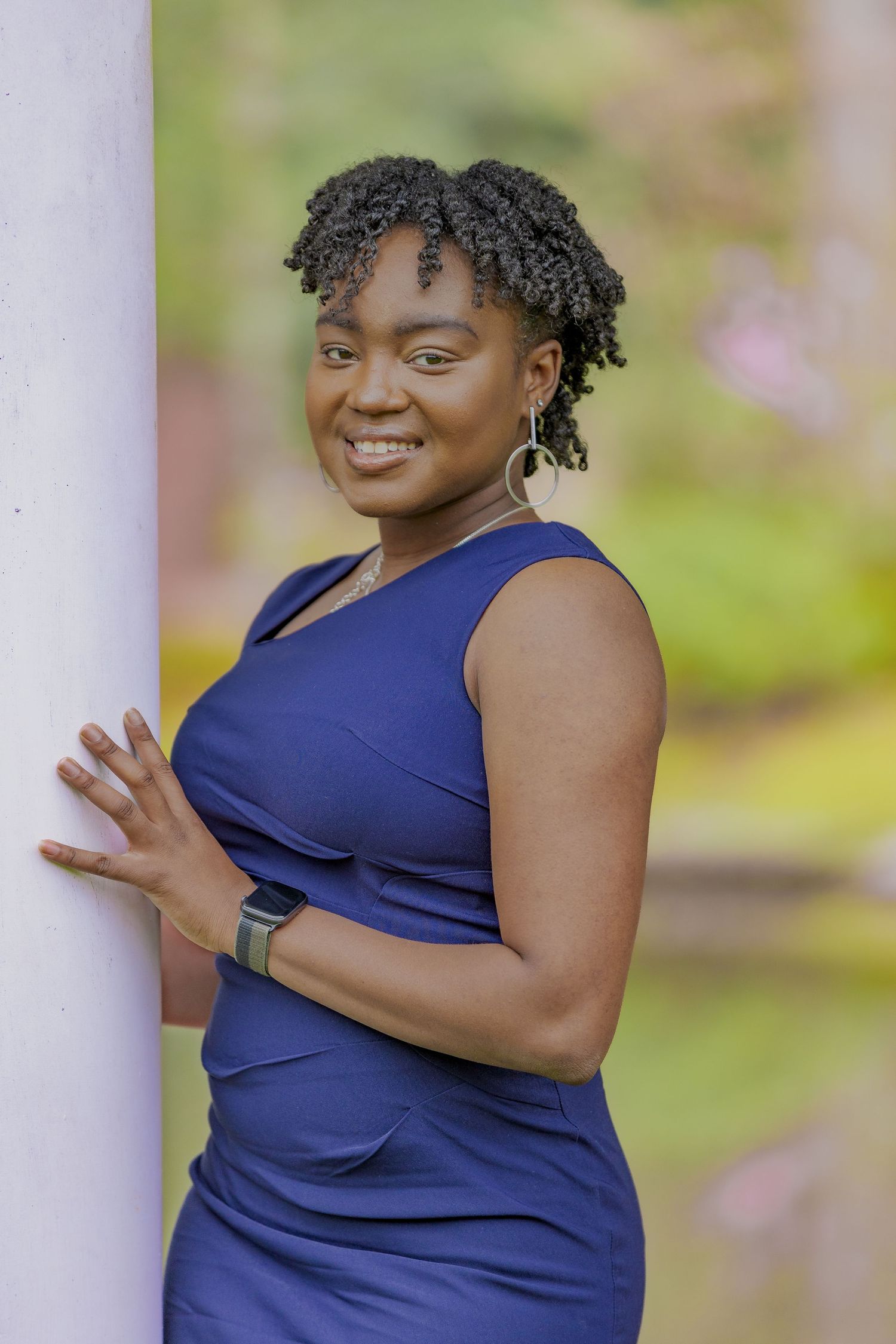 Portrait of person in navy sleeveless dress posing against white column outdoors.