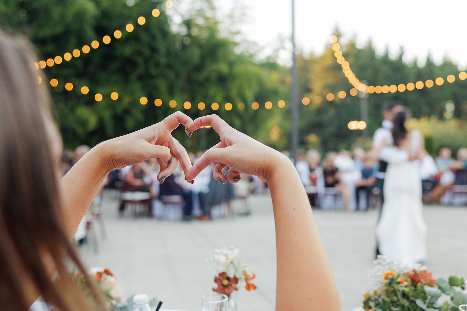 Outdoor wedding reception venue decorated with string lights and tables set for dining at dusk.