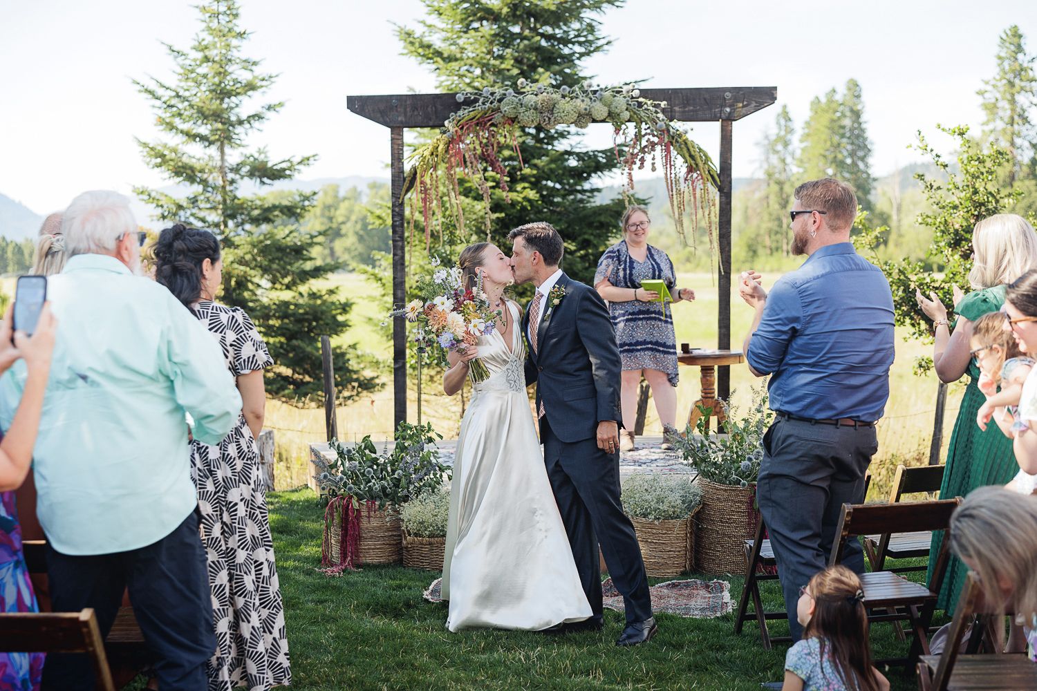 Guests gathering at an outdoor wedding celebration with evergreen trees and mountain scenery in the background.