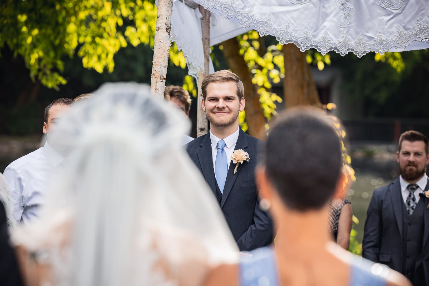 A joyful wedding ceremony moment under a beautiful canopy with green trees in the background.