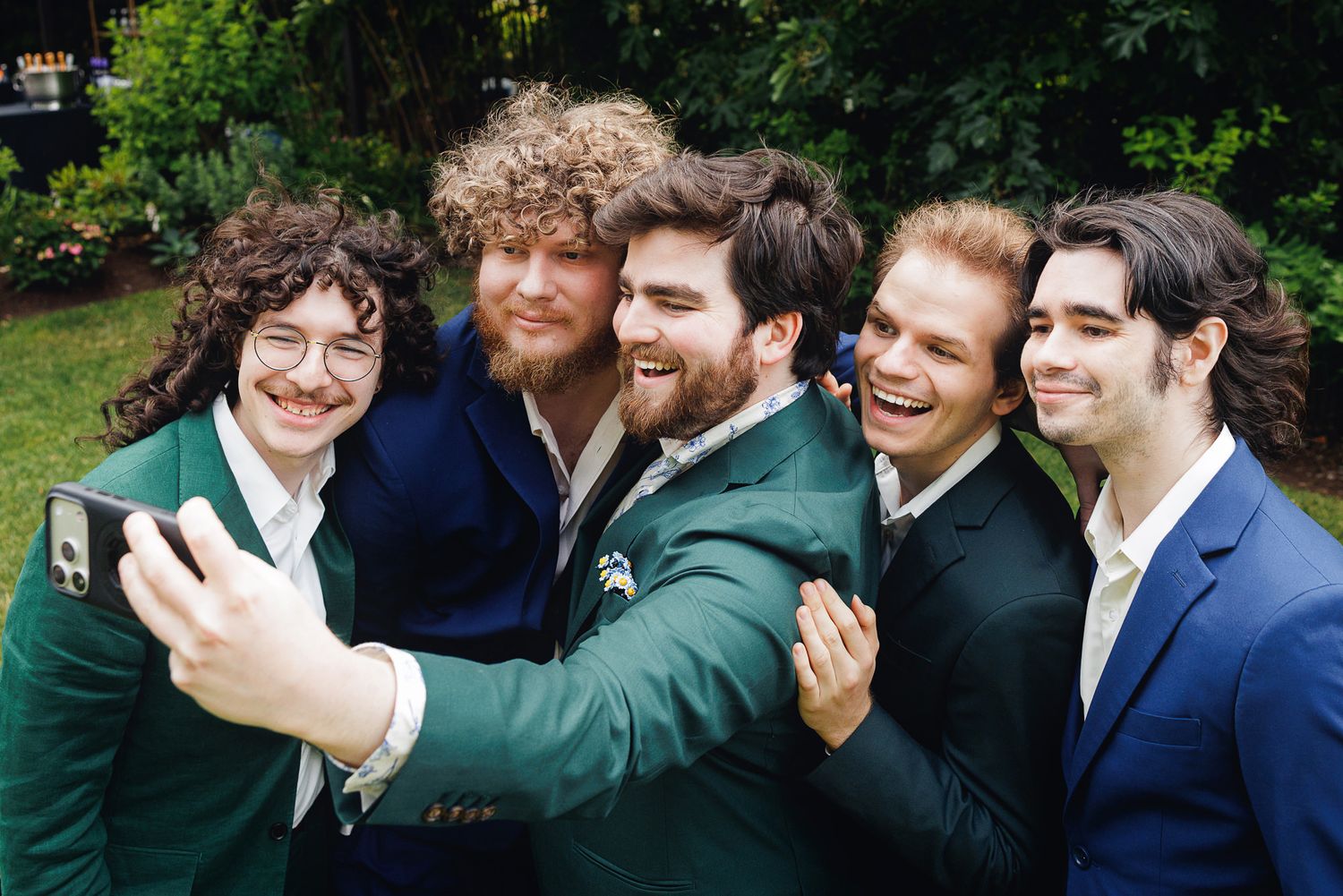 Five young men in suits taking a group selfie outdoors, smiling and posing together at a formal event.