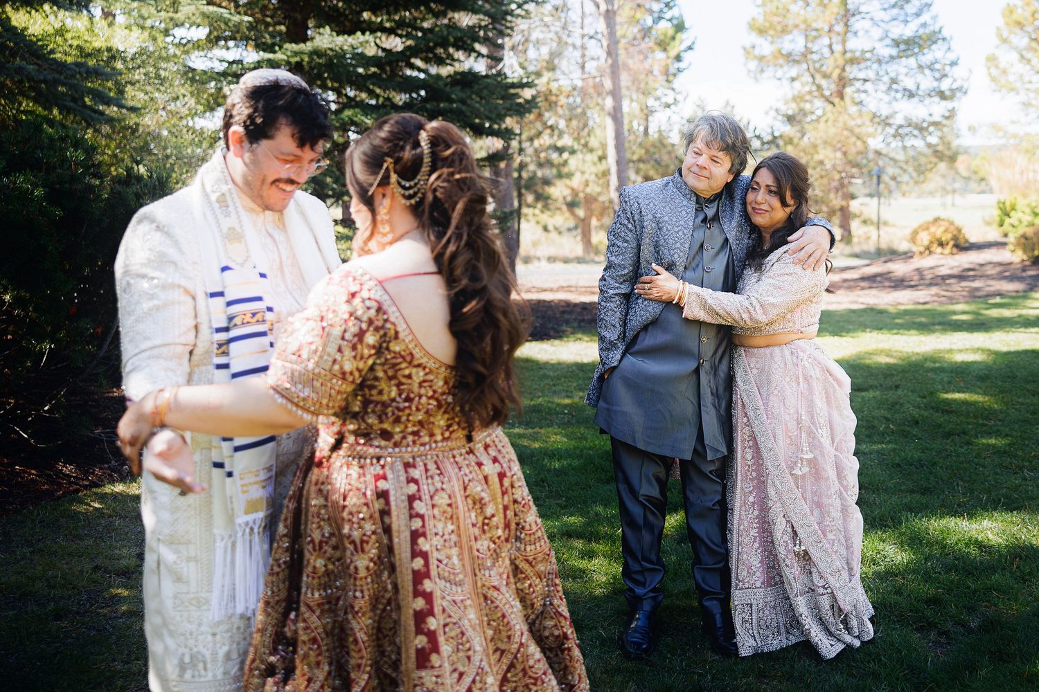 Couples embrace outdoors during a Jewish wedding ceremony, with one groom wearing a tallit prayer shawl.