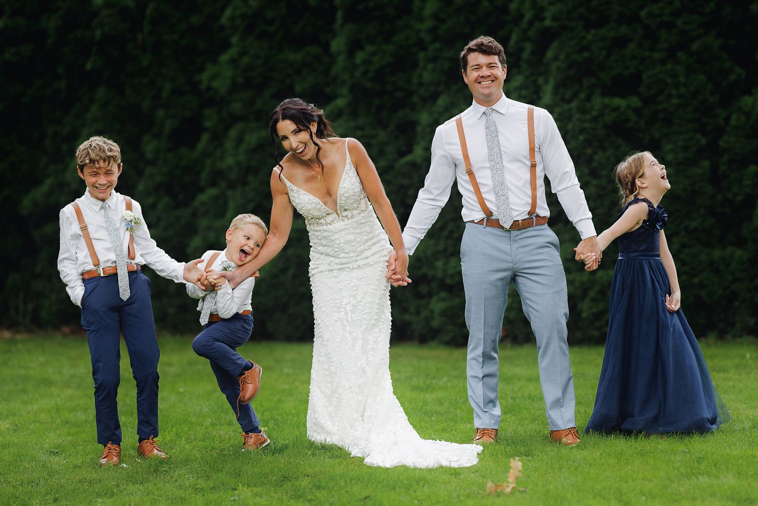 Wedding party in navy and white attire playfully poses on grass in sequence of candid jumping shots.