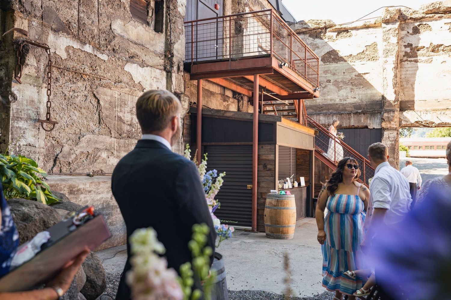 People gather at a rustic venue with stone walls and modern architectural elements in an outdoor setting.