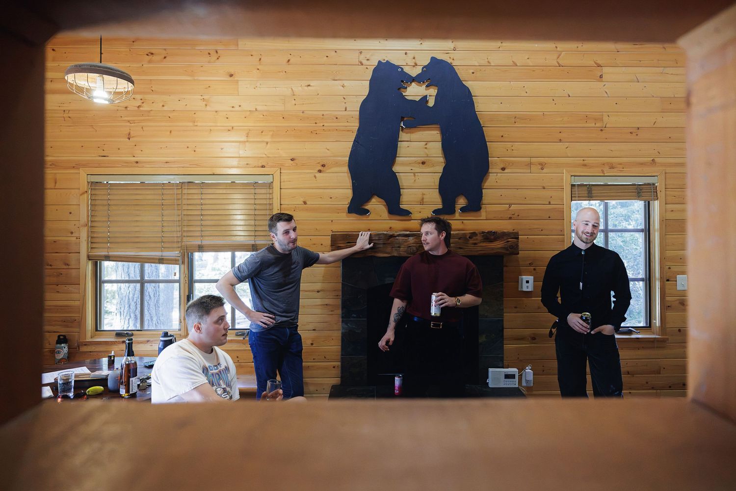 Four men gathered in a rustic wood-paneled cabin with bear wall art above a fireplace.