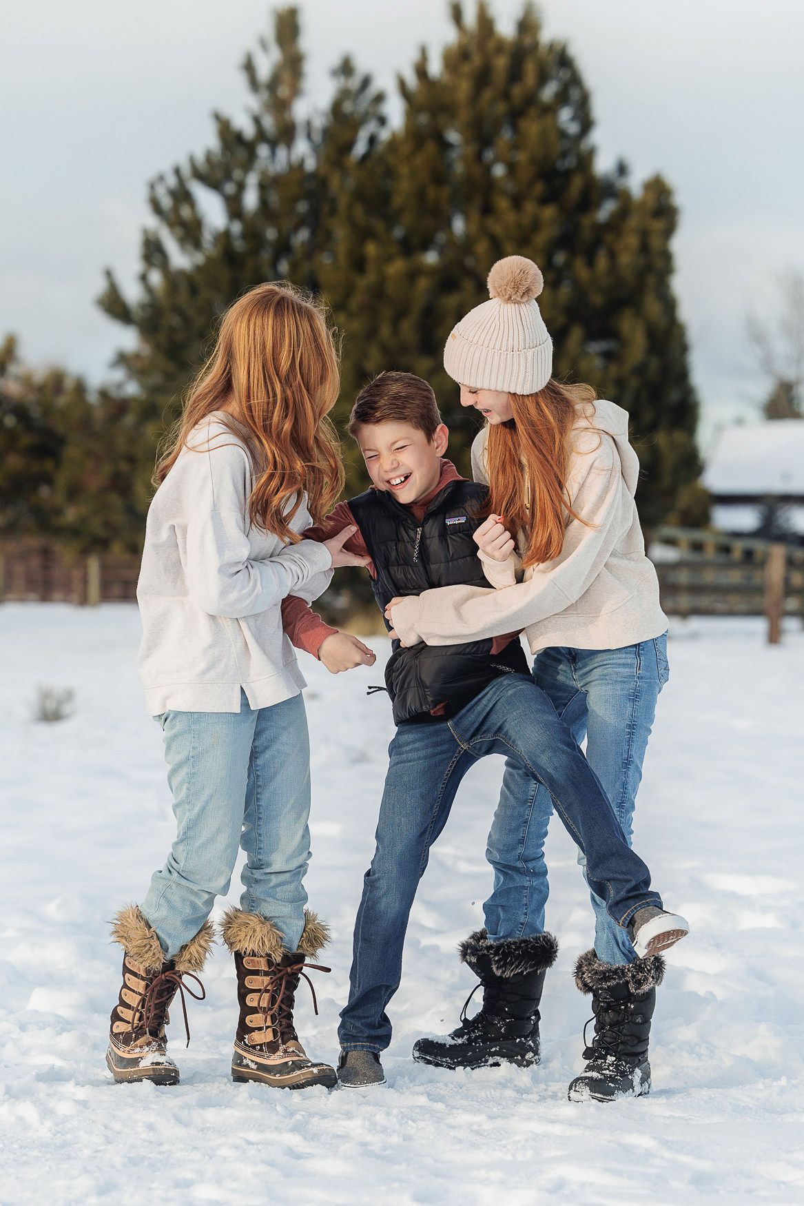 Three friends in winter clothing laughing and playing together in the snow on a cold winter day.